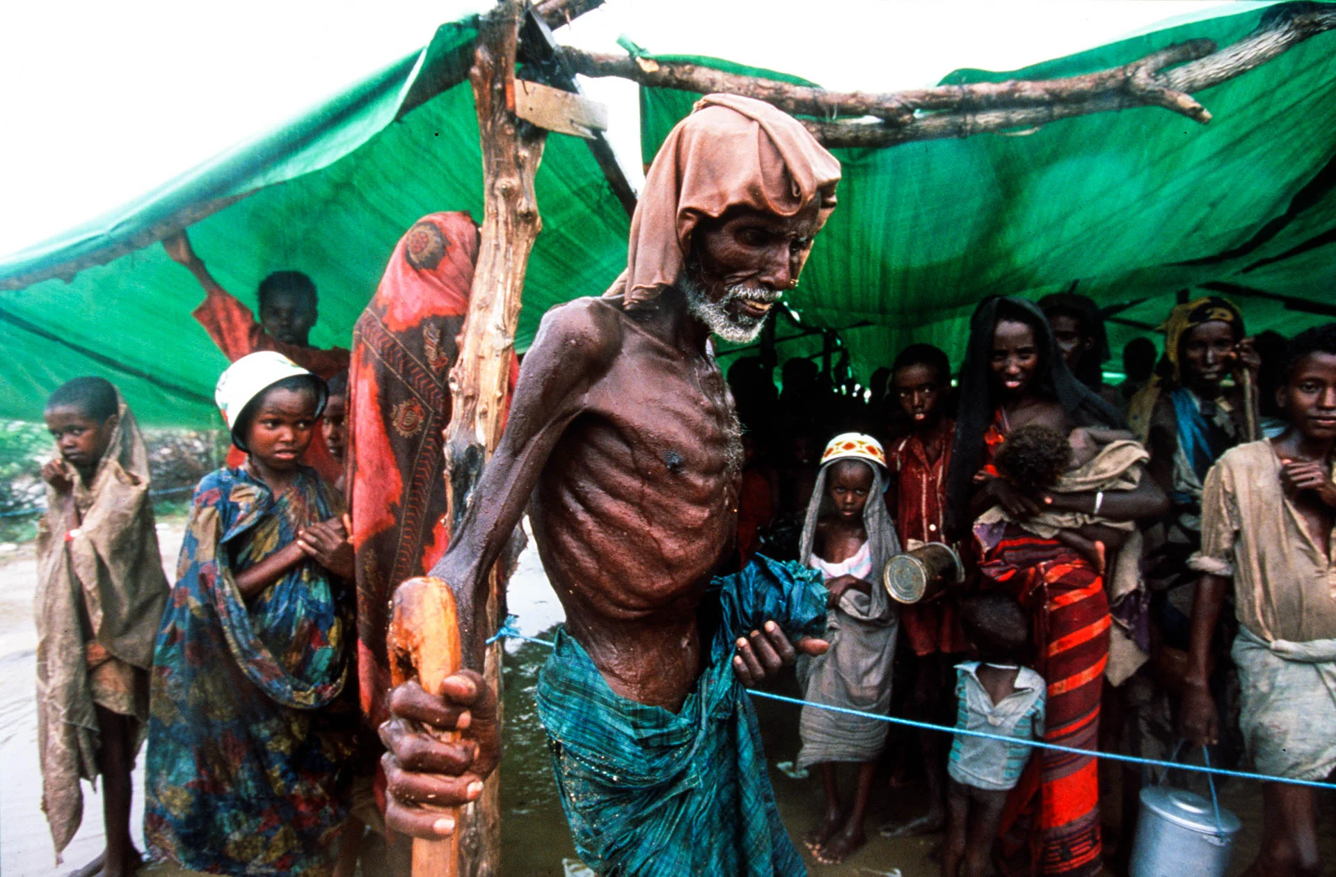 Bardera, Somalia - December 1992 An old man, some children, women. Everyone brings a pail to fill, everyone hopes that food will come soon to the Bardera refugees.