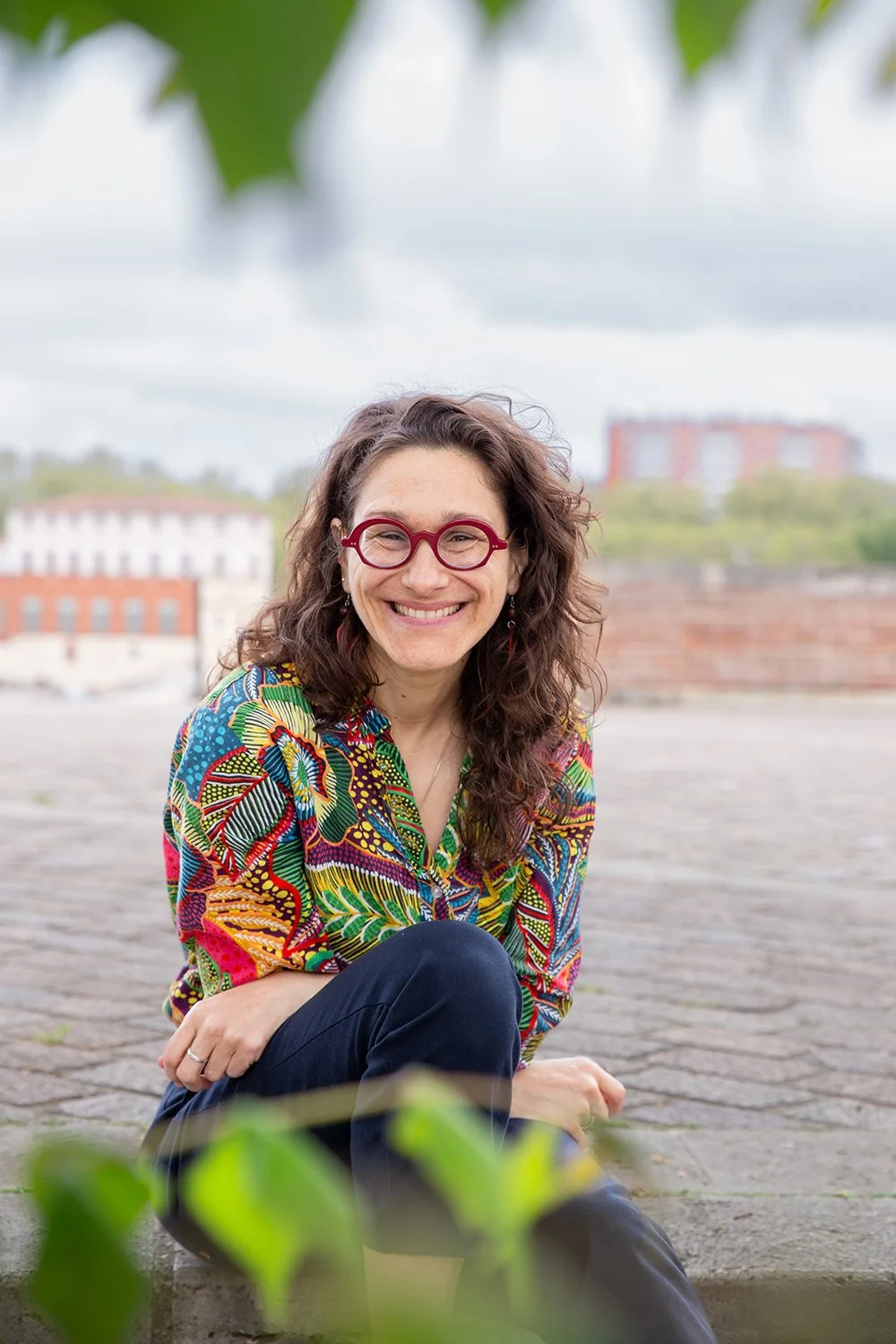Jess Vogt El, coach in Lyon, smiling, partially covered by leaves in the foreground