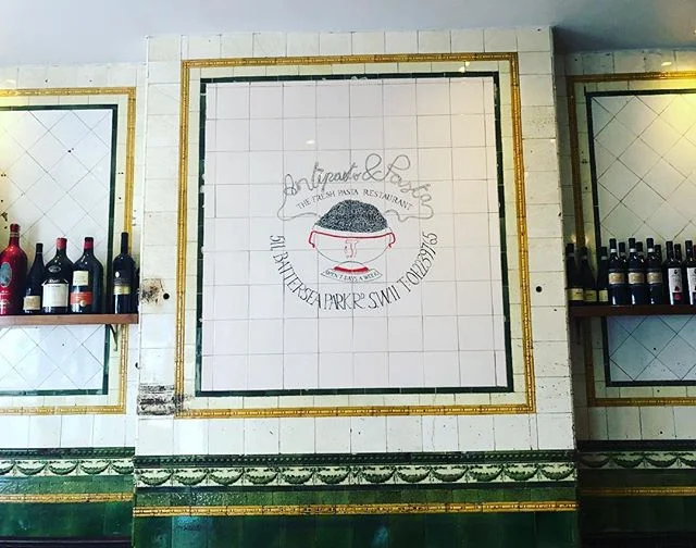 L&rsquo;Antipasto&rsquo;s doors opened in 1984 but before that it was a family run butchers. The original tiles on the wall still remain but added to it is our logo, which was designed by one Enzo Apicella, a famous artist and interior designer for o