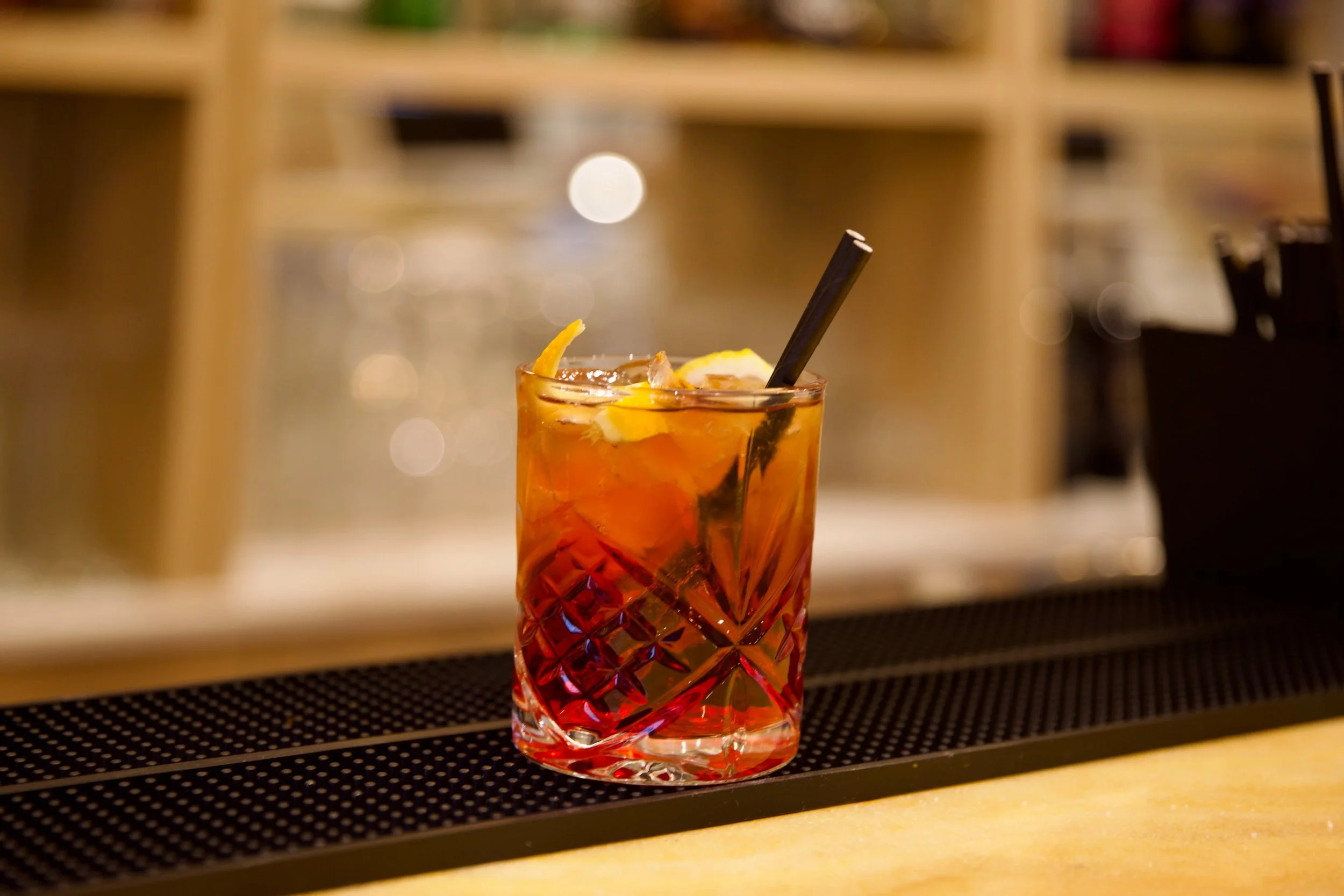 A glass of iced tea garnished with lemon slices and a black straw on a bar counter.