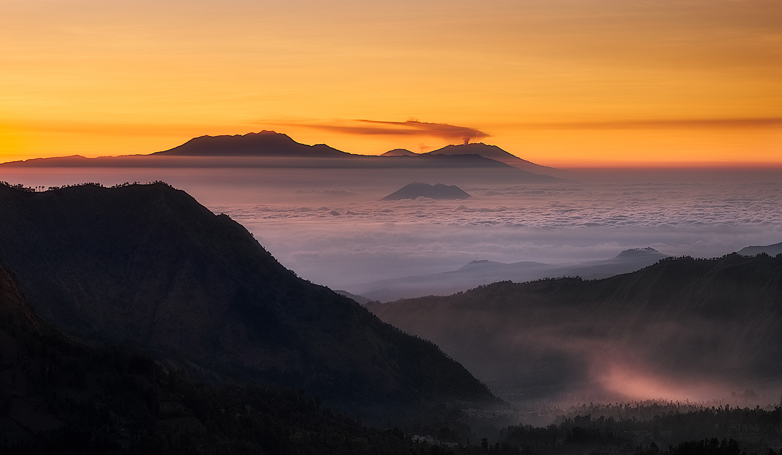 East Java Sunrise Looking east from Penanjakan on the Bromo crater as the sun rises across the volcanos of eastern Java. The small peak surrounded by cloud is the Gunung Lembongan and behind that and to the left is the 3000m Gunung Argapura. Behind that is the smoking Gunung Raung, the volcano that disrupted so many flights to and from Bali in August and September 2015. It's about 120km away from where we were standing.