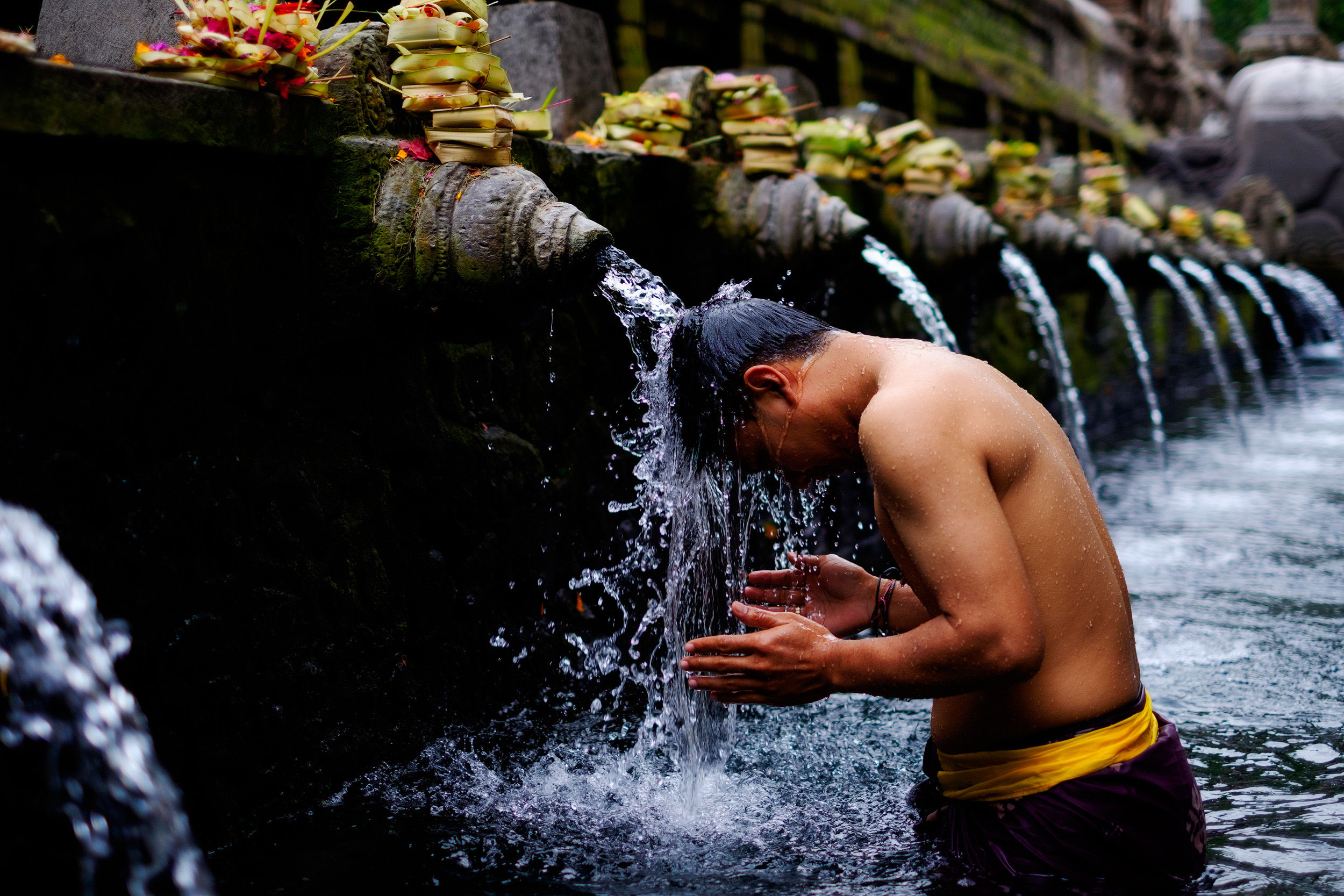 Tirta Empul People travel from all over Bali to bathe and sanctify themselves in the spiritual waters of Tirta Empul. According to legend, the God Indra pierced the earth to create a fountain of healing waters after the land had been poisoned. People bathe and leave offerings on top of each fountain as they work there way down the pool. It’s a wonderful place to spend a few hours in the morning. I had to put on a sarong and get into the water to get this shot.