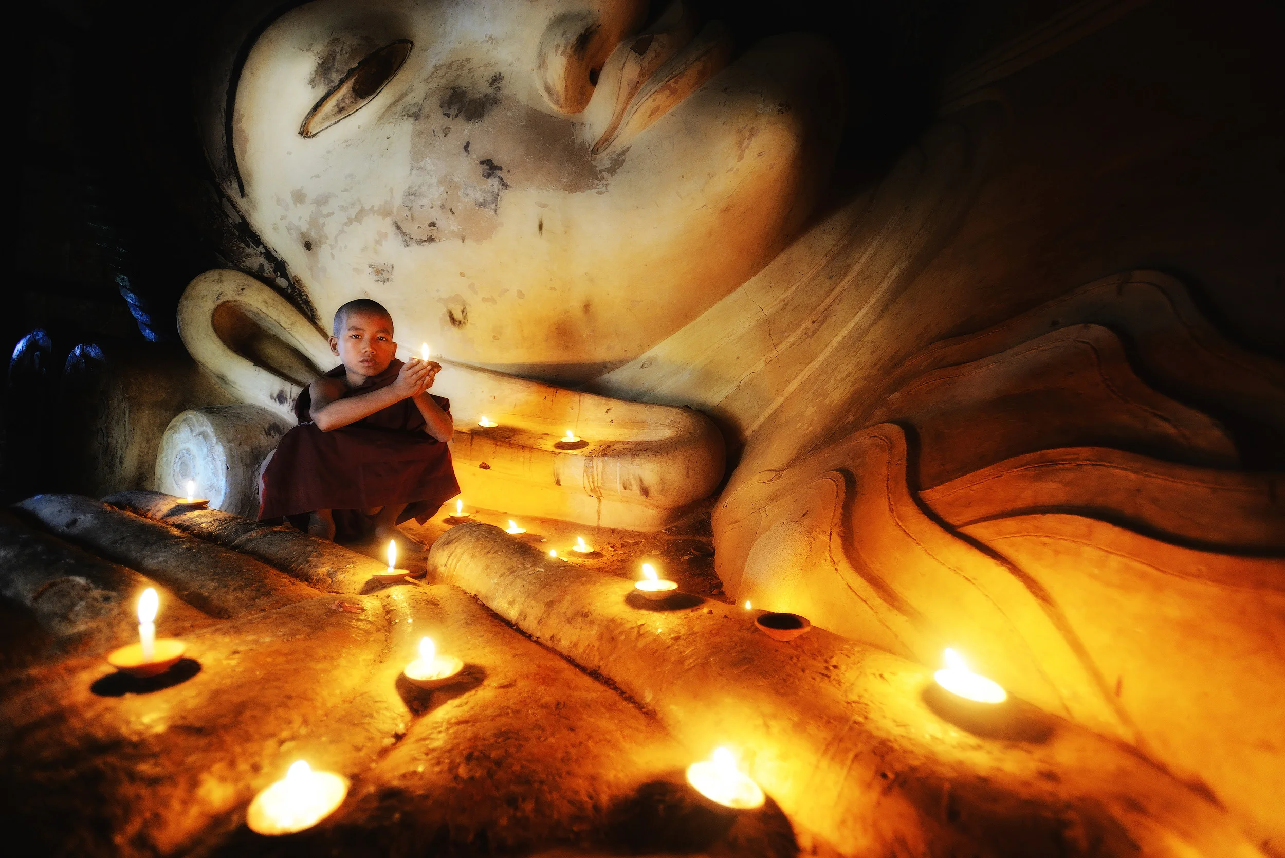 Prayer A shot of a novice monk in front of the reclining buddha at Shwesandaw Paya, Bagan. As we entered the tiny building where the buddha is located we came across a photographer shooting this scene. It's not a "natural" scene, as the photographer, who was shooting a book in Burma, had a guide who'd set up the scene for him complete with local novice monks who were carefully posed and lit. The photographer invited me to take a shot of the scene and even though I'm generally not a big fan of contrived posed scenes like this, I wasn't going to decline.
