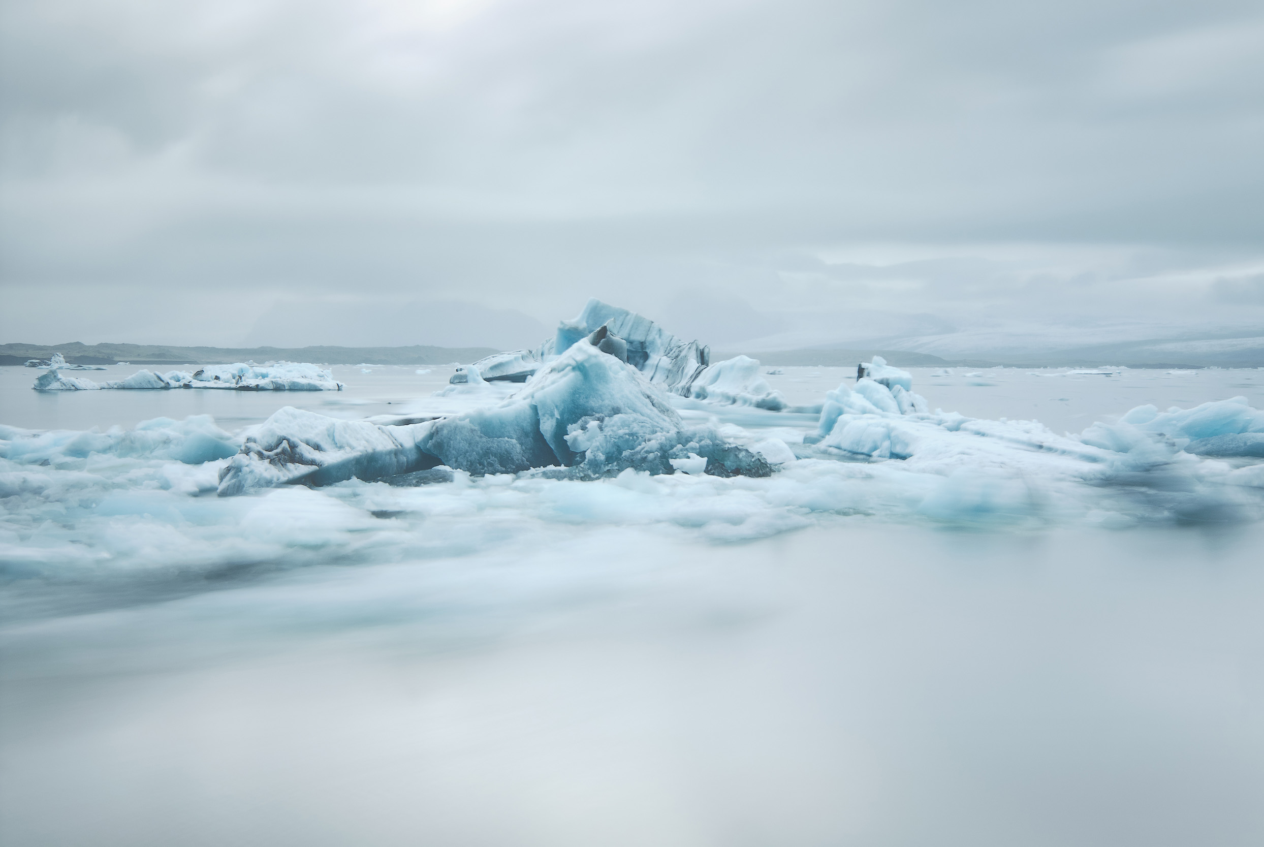 A long exposure blurs the smaller icebergs as the flow the the sea while the larger pieces remain caught on the bottom of the lagoon.