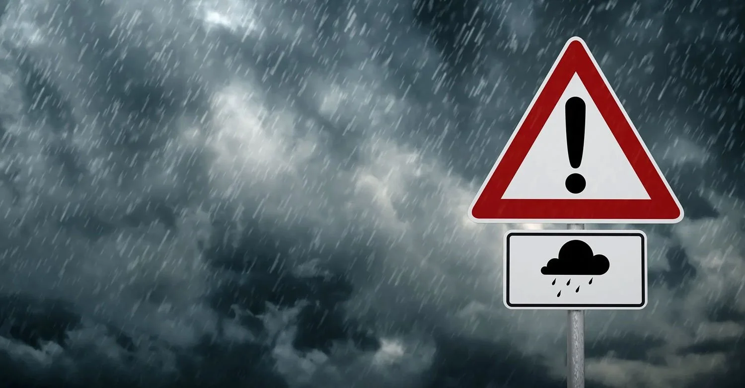 Red-and-white-triangle-shaped-traffic-sign-with-a-black-exclamation-point-set-against-a-backdrop-of-heavy-rain.jpg