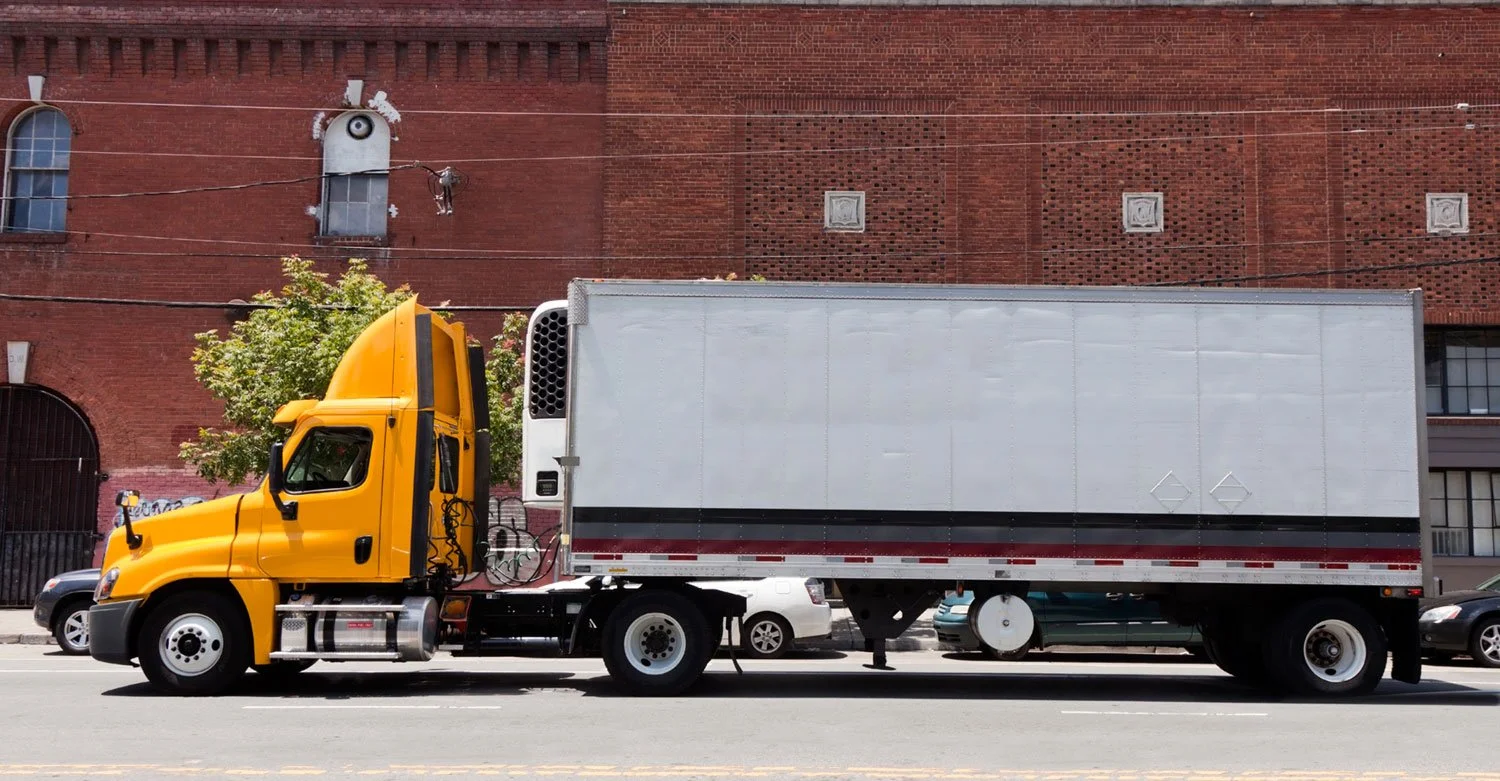 Yellow cab and refrigerated trailer parked in front of brick building.jpg