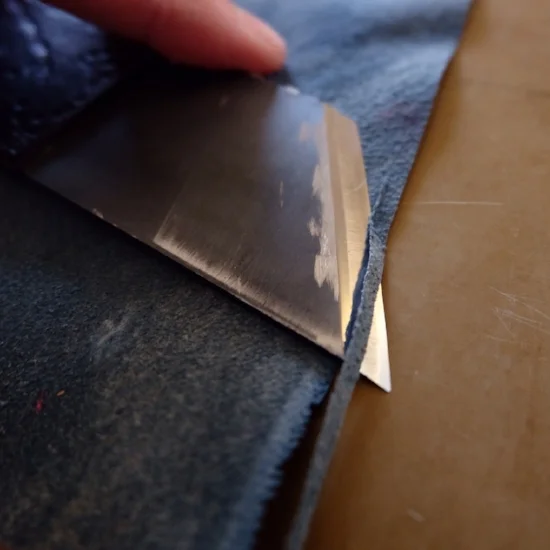 Edge paring the leather with a razor sharp knife. Paring essentially bevels the leather around its perimeter, allowing it to be easily turned in around the board edges of the book. 