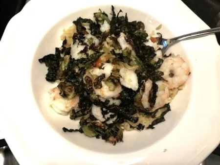 Brown rice bowl with shrimp, fish, garlic, roasted cauliflower and red onion with kale and shaved brussels sprouts as a topping.