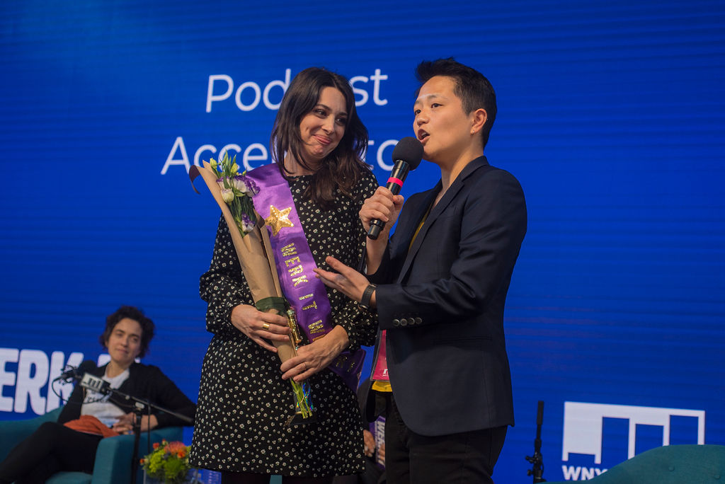 Kathy Tu presenting an award on stage to the Podcast Accelerator winner