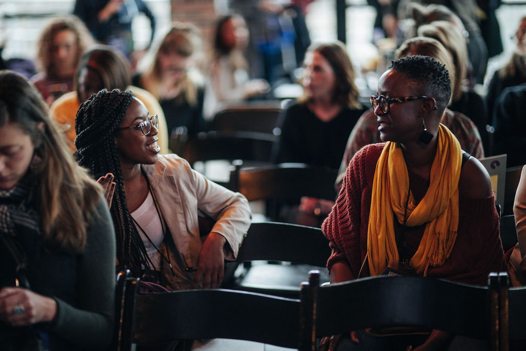 Two attendees in the audience talking and smiling