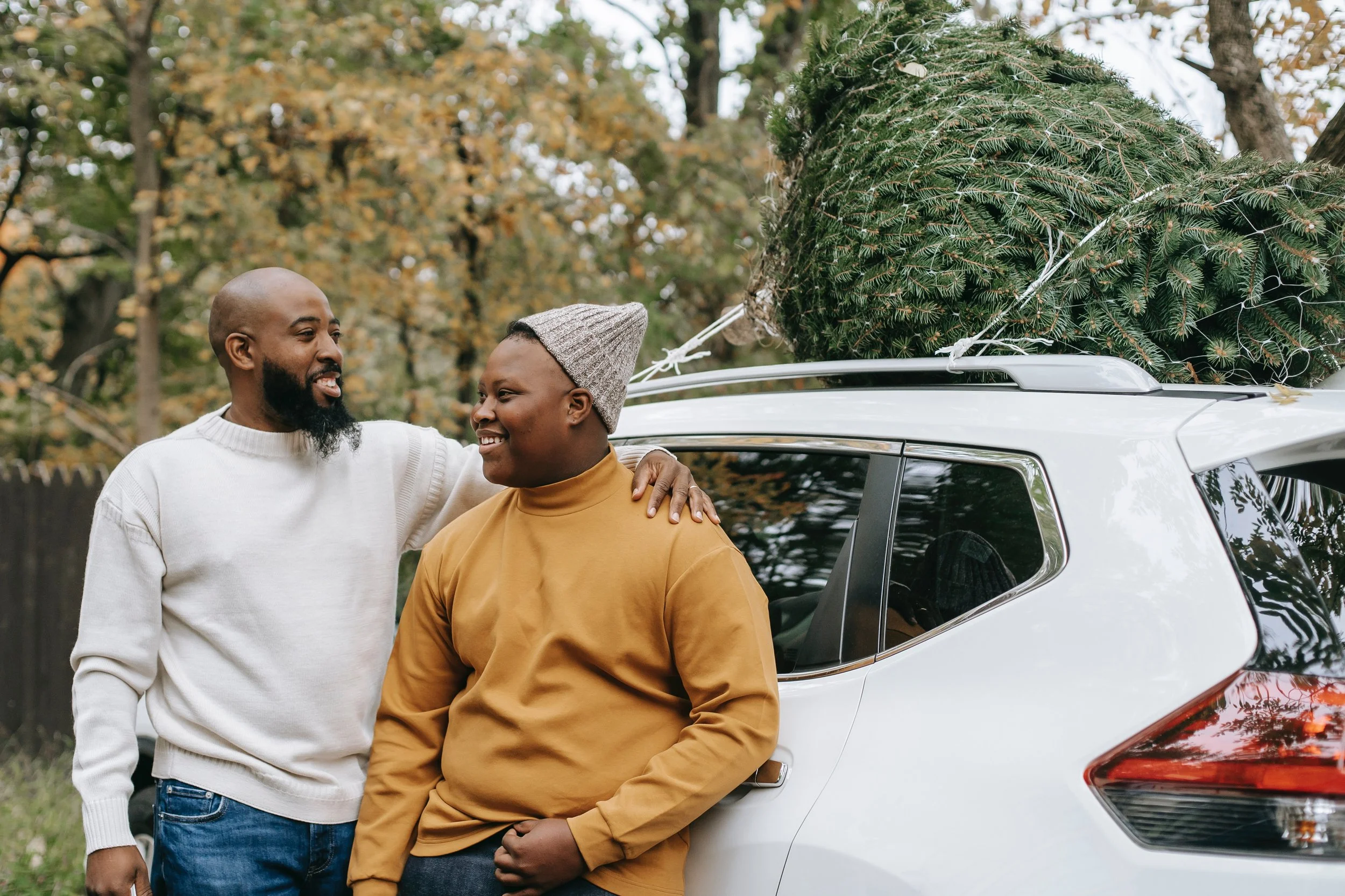 Parent talking to teenager lovingly with arm around their shoulder in front of a car with a christmas tree on top