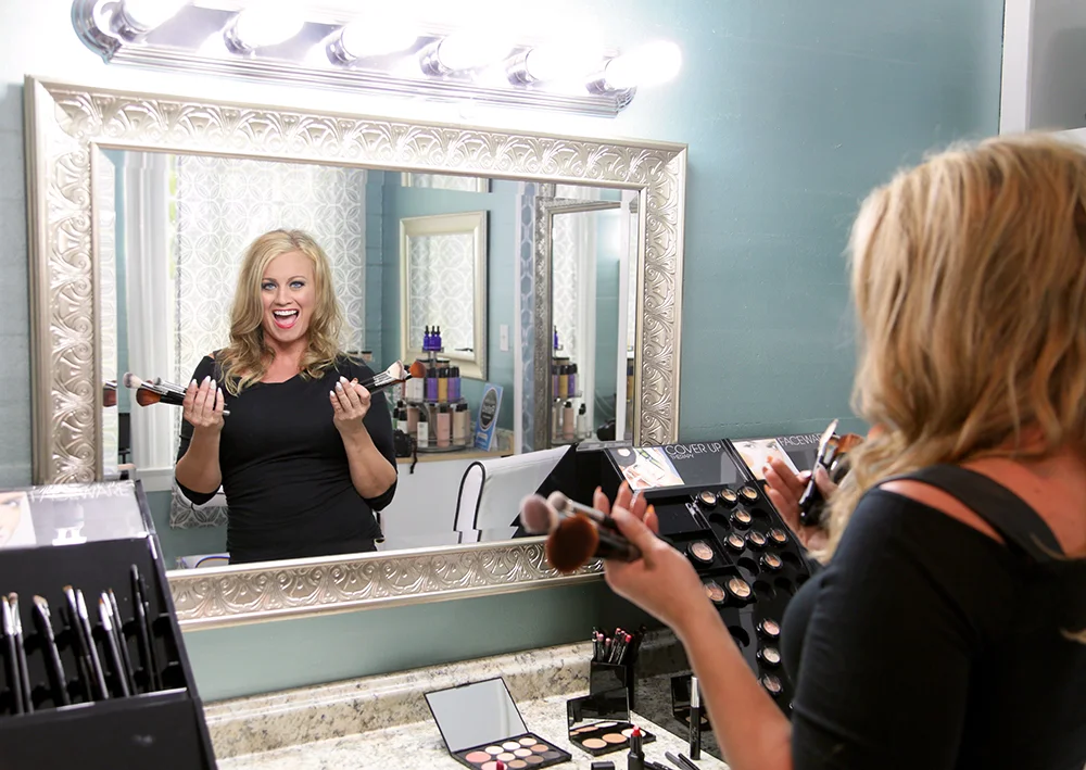 Image of Lorri Bolander founder of Key West Hair and Makeup surrounded by makeup and holding blush brushes.