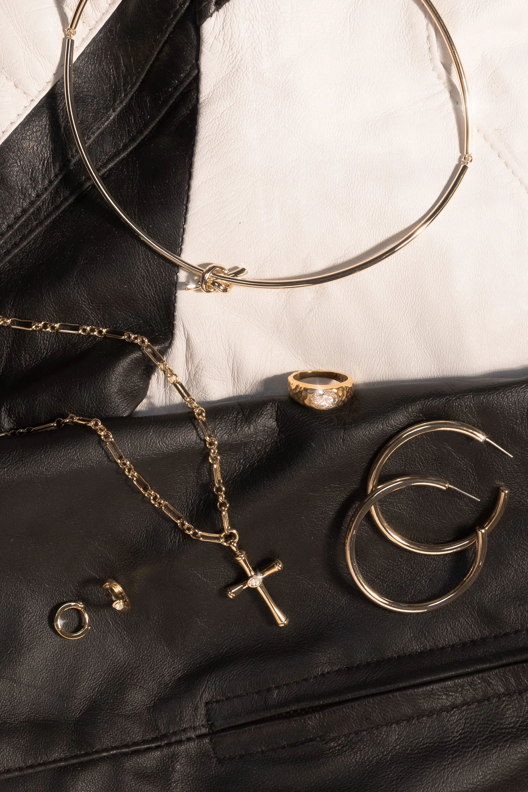 Gold and silver jewelry including earrings, a ring, a necklace with a cross pendant, and a bracelet, arranged on black and white leather surfaces.