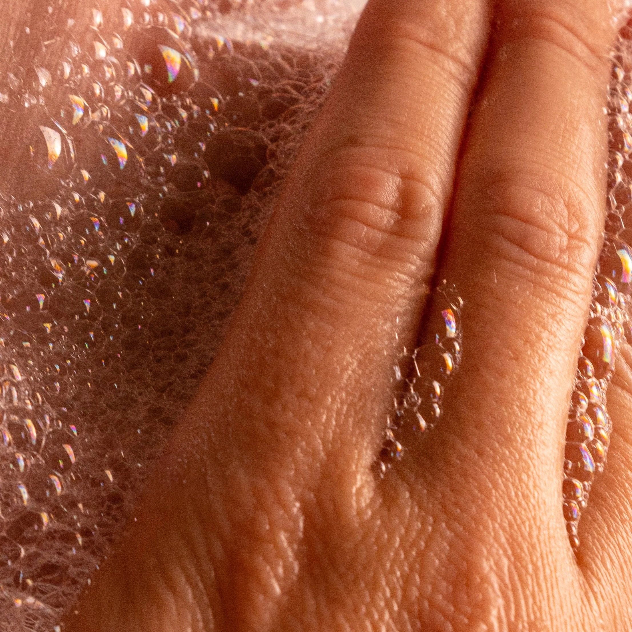 A hand pressing down on soap bubbles, causing them to bubble and reflect light.