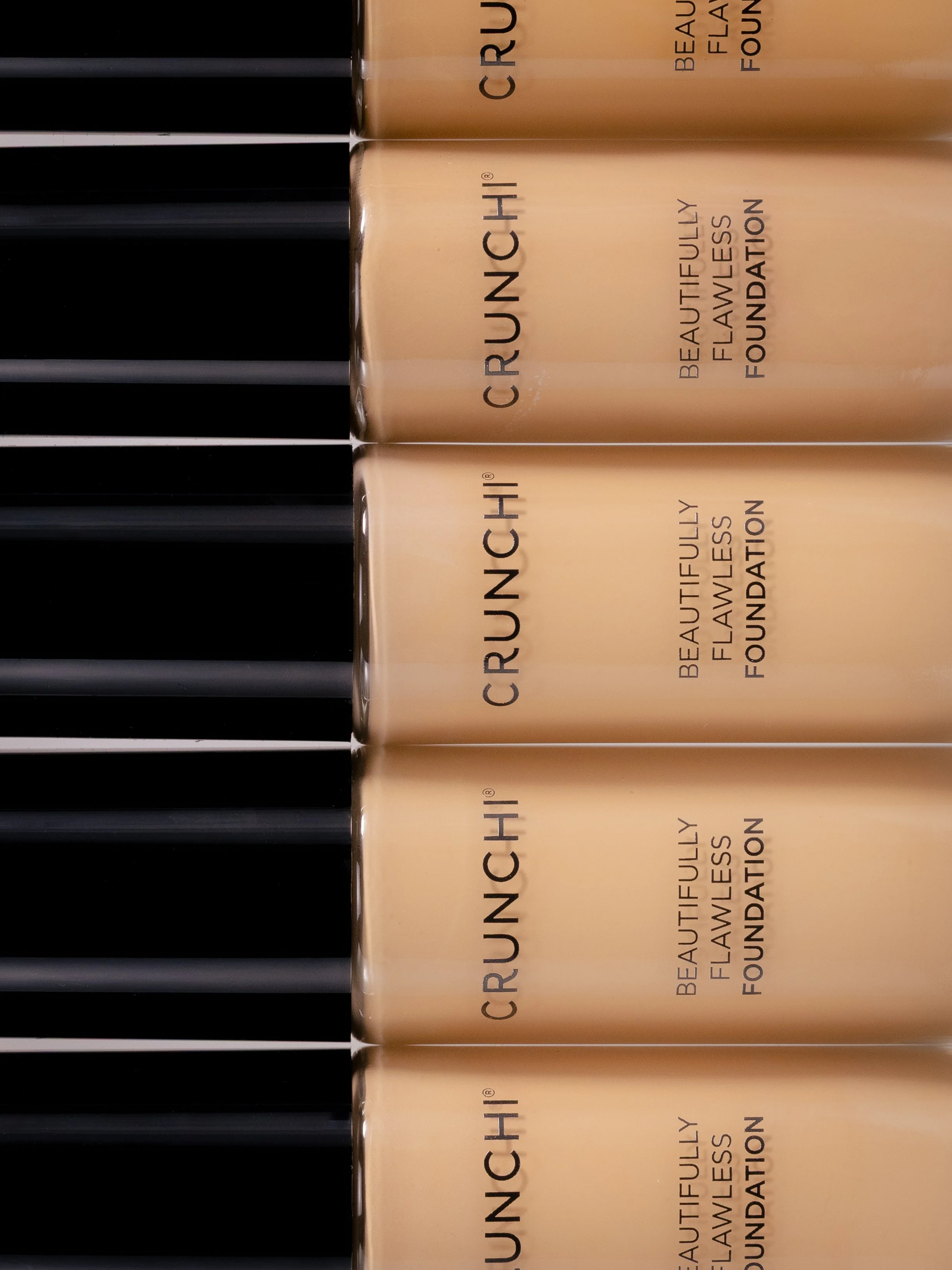 Clean beauty product photo of multiple bottles of Crunchi Beauty Flawless Foundation arranged in a row, showing their labels.