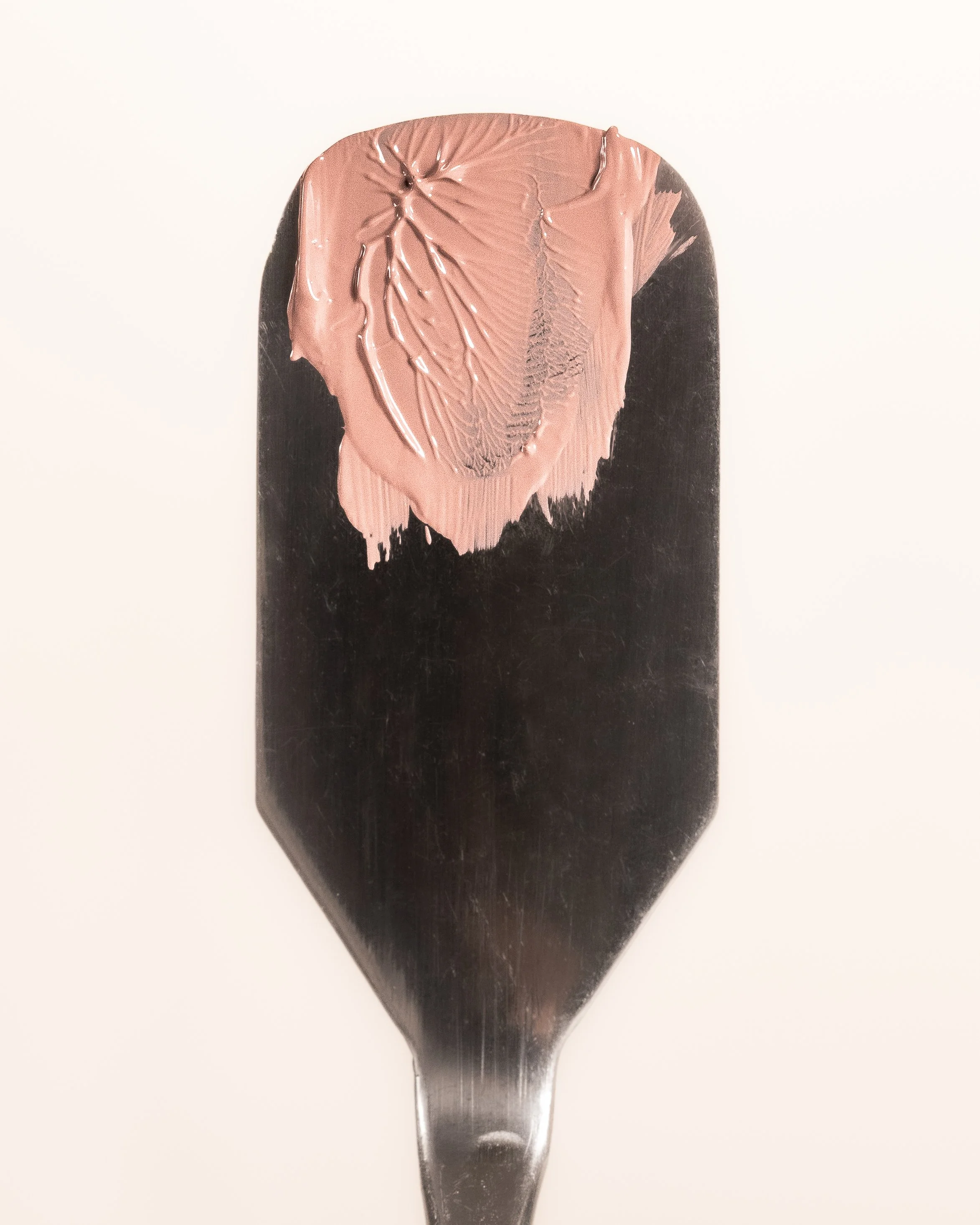 A paint palette with pinkish-beige paint partially spread across a black surface.