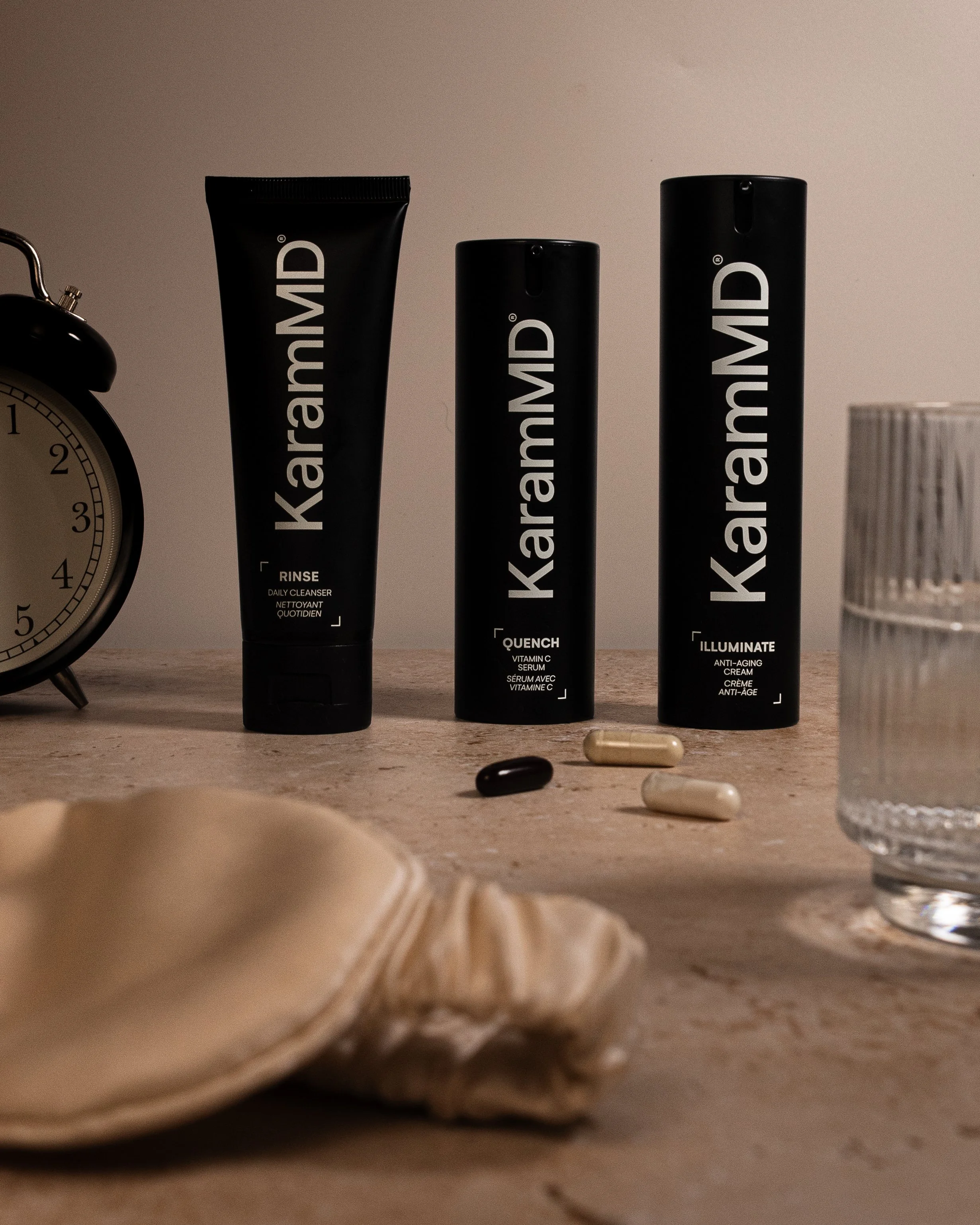 Kiehl's skincare products on a wooden surface, including a rinse daily cleanser, Vitamin C serum, and anti-aging cream, with pills, a glass of water, a clock, and a shell nearby.