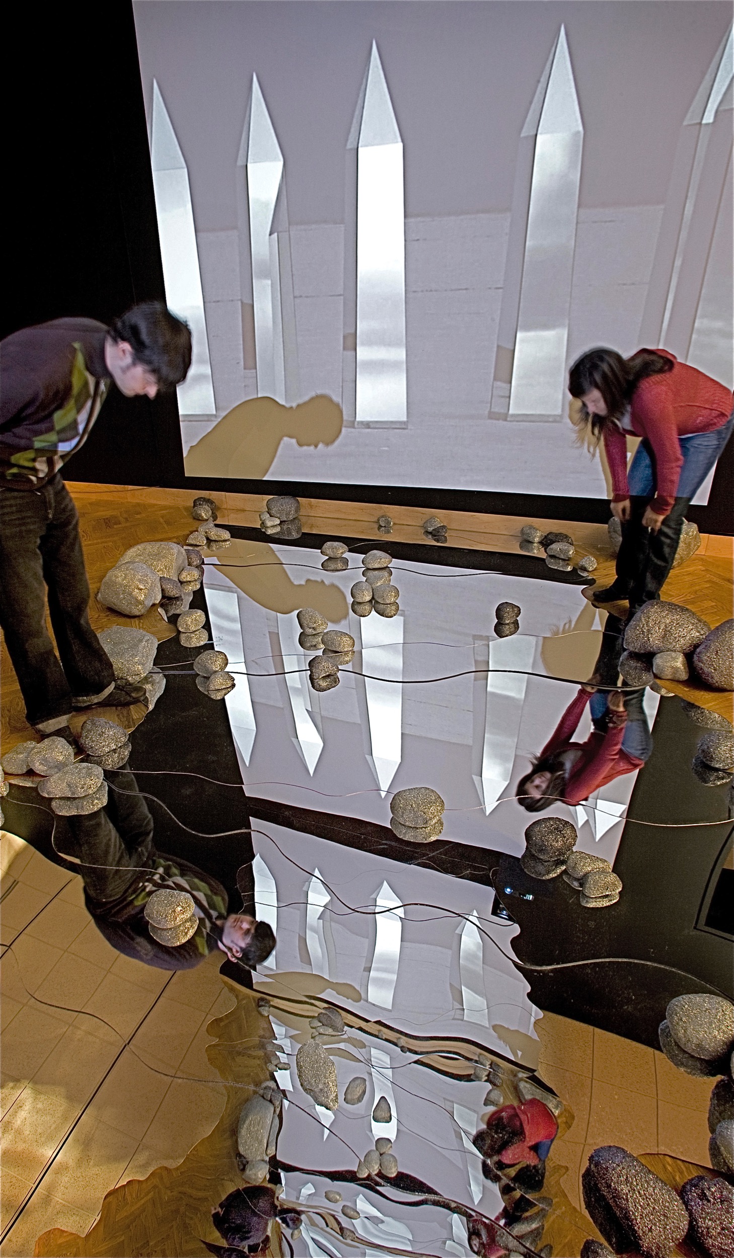 infinity space between the symmetrical mirrored rivers on the gallery floor and ceiling shows the 2 channel video reflecting and the reflections of the visitors (detail)