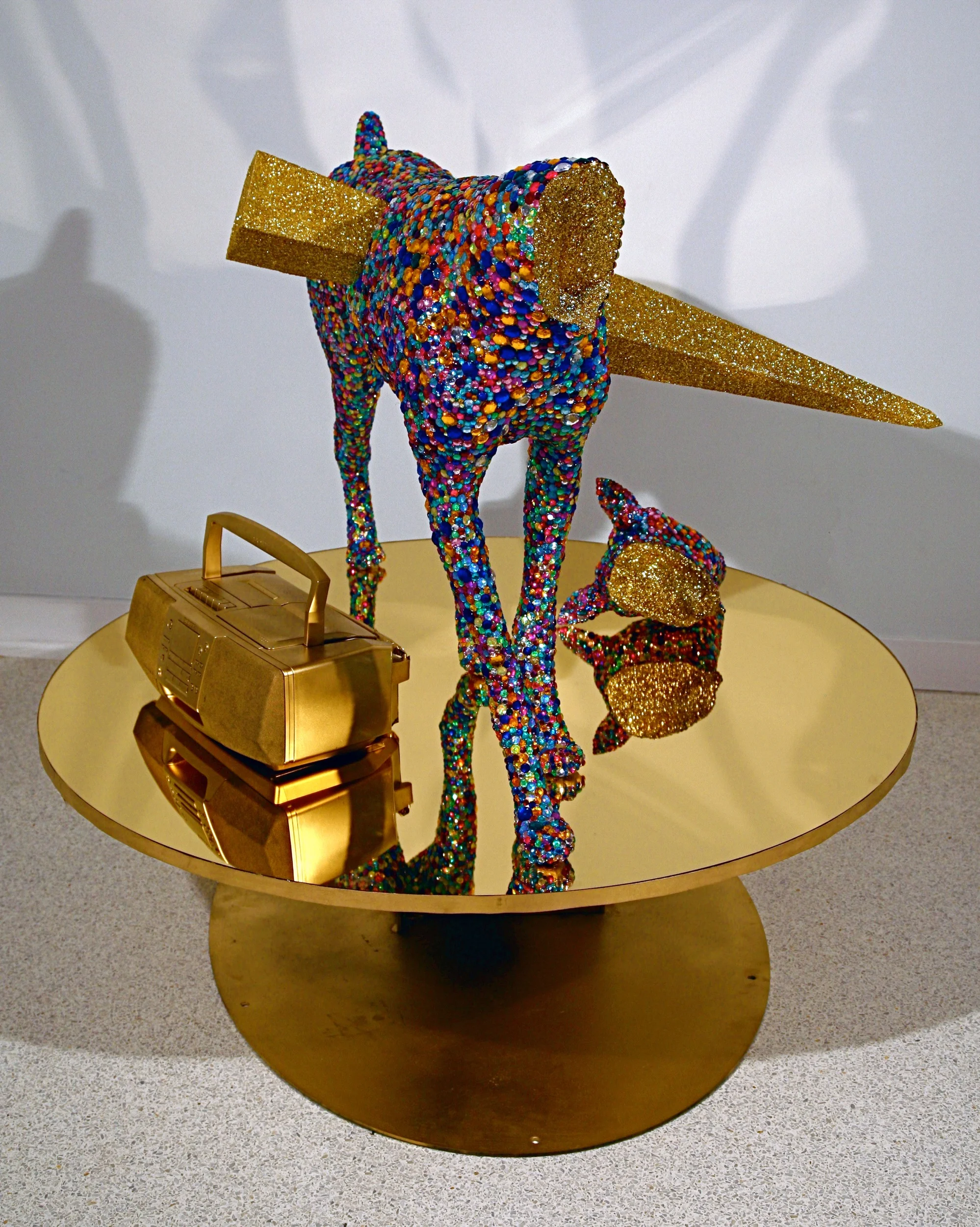  Diamond Dog , 2009, mirrored acrylic sheet, mdf, cast polyurethane, epoxy resin, glass eyes, acrylic rhinestones, Sony boom box, enamel paint, sound, 66” x 48” x 48” Diamond Dog incorporate references to the Sex Pistols, using sound to recontextualize dystopic phrases and address the failures of utopian ideals while exploring reflection as a tool to draw the viewer into the work. The reflection allows the viewer to explore their own position in history and culture and points out the futility of utopian desires.