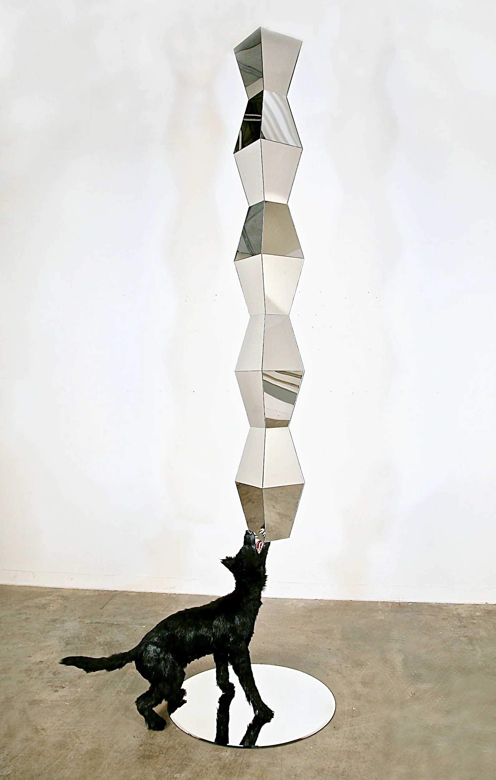 Broken Column , 2013, mirrored acrylic, cast polyurethane, fur, mirrored glass, steel, mdf, 114" x 30" x 40" The title is a satirical homage to Constantine Brancusi’s monument The Endless Column -- considered one of the seminal sculptures of modern art. Made of mirrored rhomboidal modules -- a taxidermied coyote is either holding the column up or pulling it down into the mirrored surface below the coyote.