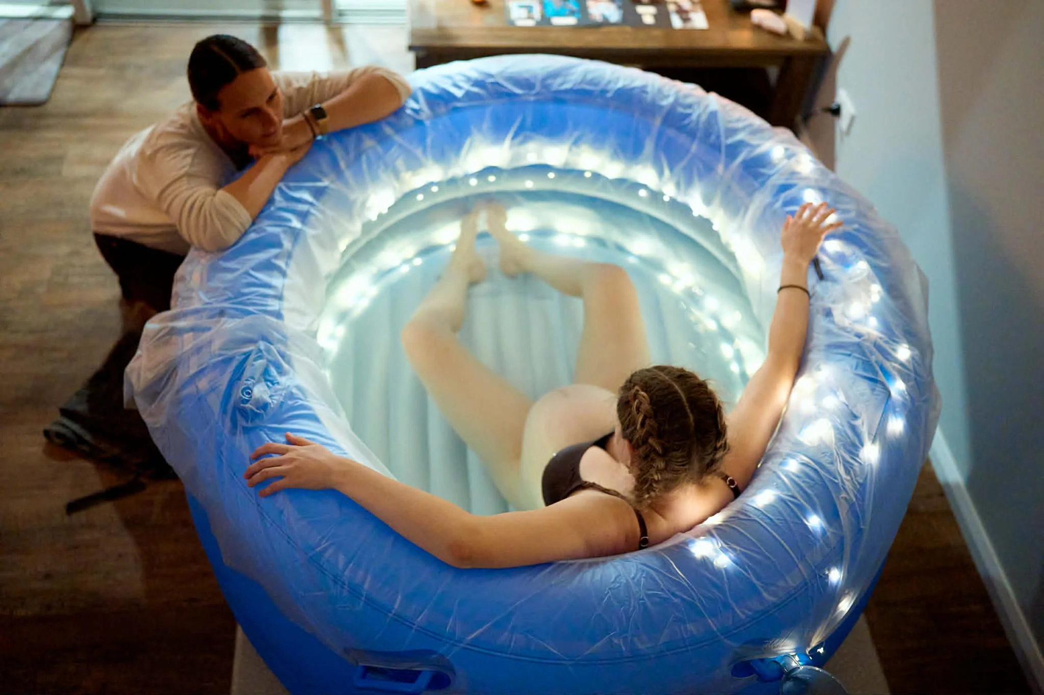 Woman birthing at home in inflatable birth pool with fairy lights supported by her doula Nancy McLean