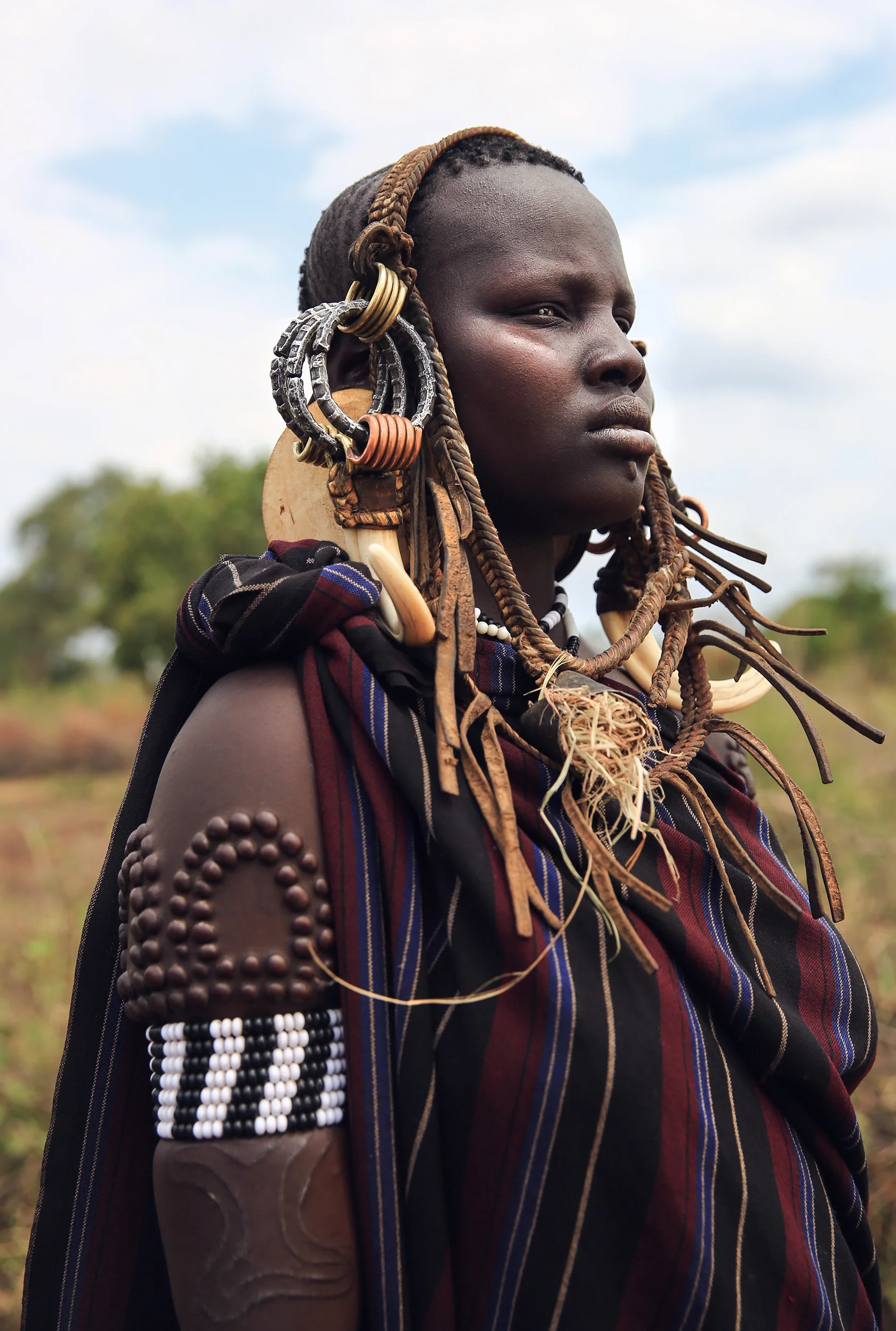 The sign of beauty among Mursi women are large lip plates and scarification, sported by almost all of the adult women. When a Mun (as they call themselves) becomes engaged to be married, usually around 14 or 15, she disappears from village life to live in her family hut. The gap between her front lip and the flesh below is pierced and gradually stretched. In the beginning a hole is made in the lip with a wooden stick. The stretching continues as successively bigger discs of clay or wood are accommodated by the changed lip. Generally the two lower front teeth are pulled or knocked out to aid in the process. The final size of the plate helps to determine her beauty & bride price.
