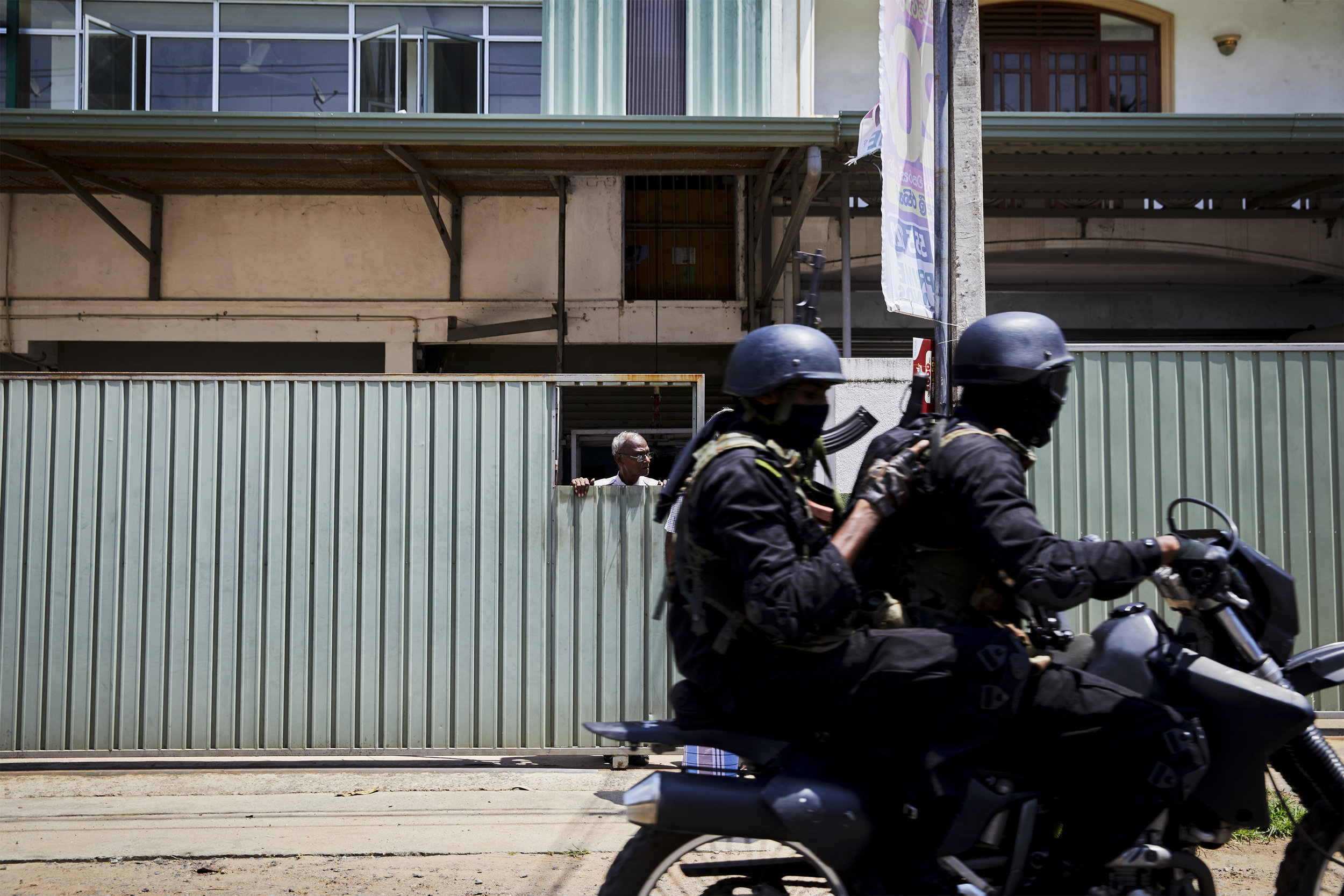  A resident of the Kolpititiya neighborhood, the site of one of eight bombs detonated on Easter Sunday, watches as special forces race by on motorcycles. The  military and police presence during the days after the terrorist attacks were numerous  Col