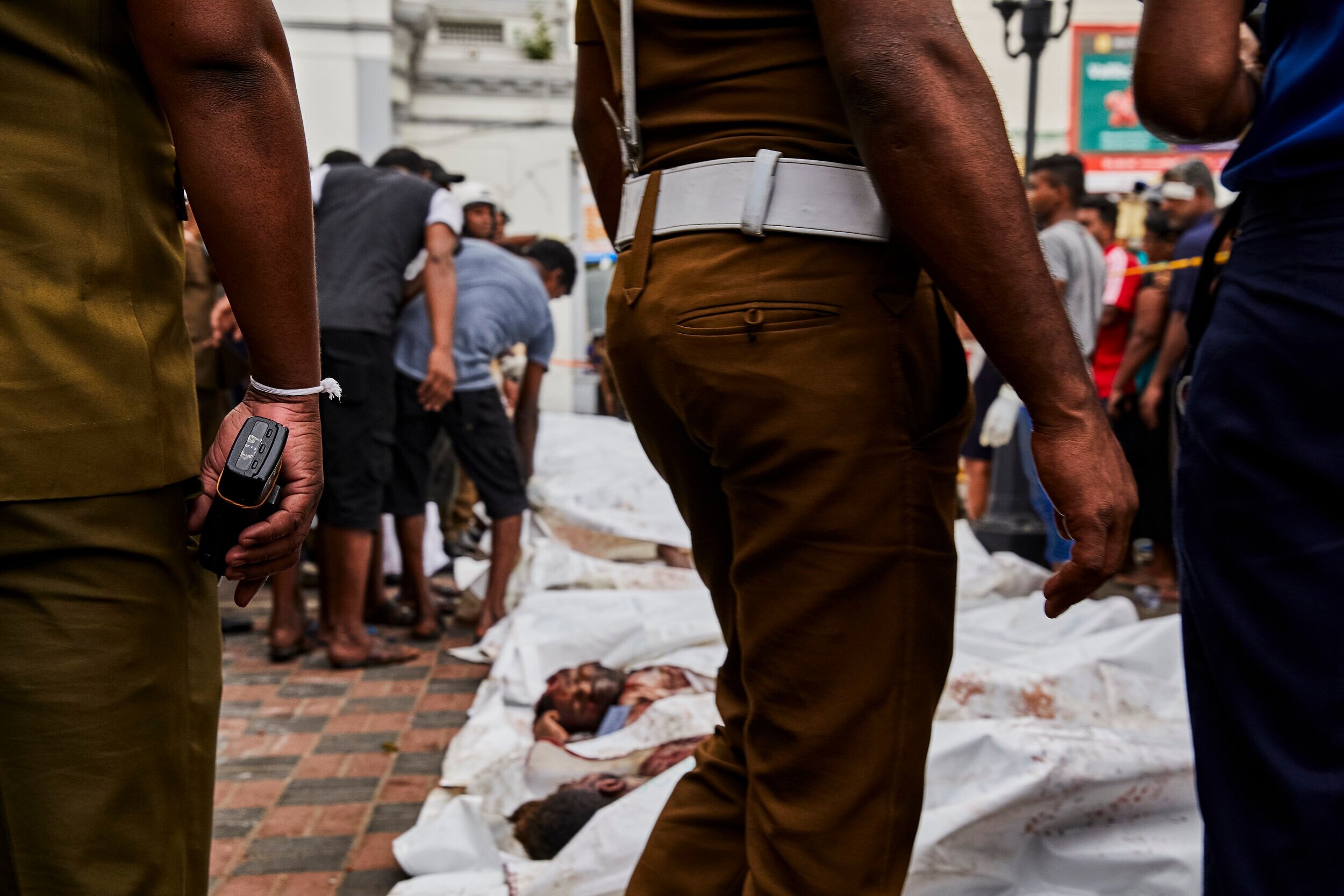  Police stand guard as the remains of those killed in the suicide bomb explosion at St. Anthony's Church are laid on the sidewalk. The bodies have been uncovered so they can hopefully be identified by any family members in the growing crowd, which pr