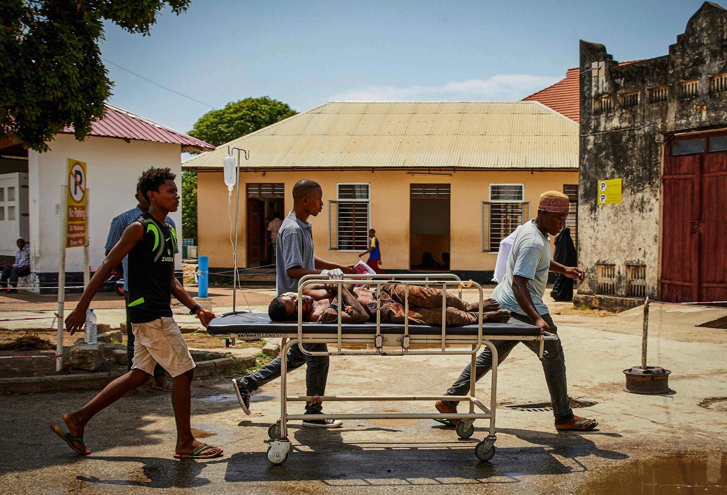  Male relatives move a gurney with a sick patient across the yard at the Mnazi Mmoja hospital.   At government hospitals in Zanzibar, everything- including bedsheets, daily meals, physical washing, and transporting of the patient to different departm