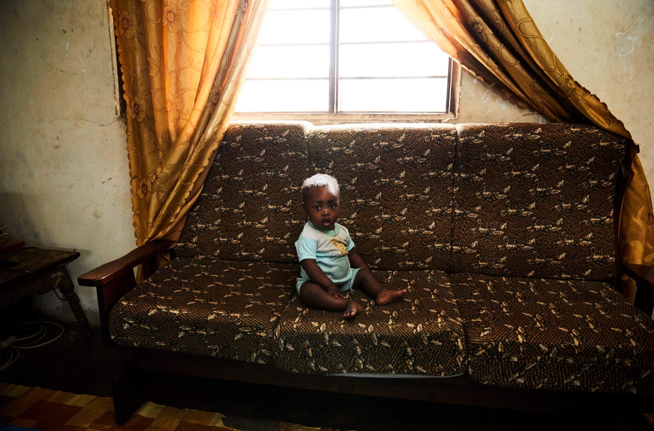  1 year old Nurdiin, born with Down Syndrome sits on the couch of his home. He is the youngest child of his 43-year-old mother, Salha Abdallah, who has 7 children in total including him.  The two of them go twice weekly to  Mwanahija Mzee’s tradition