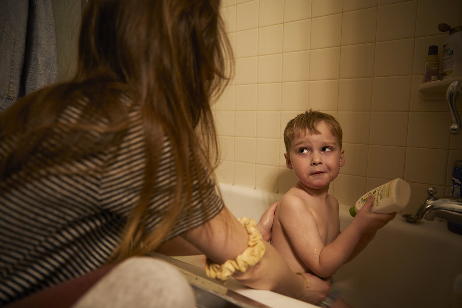  Kathleen  bathes her 3 year old son Gabriel, while explaining why he shouldn’t squirt the entire bottle of soap into the tub.  Due to the Covid-19 pandemic, Kathleen has no childcare help, as even daycares were closed. She feels intensely bad for he