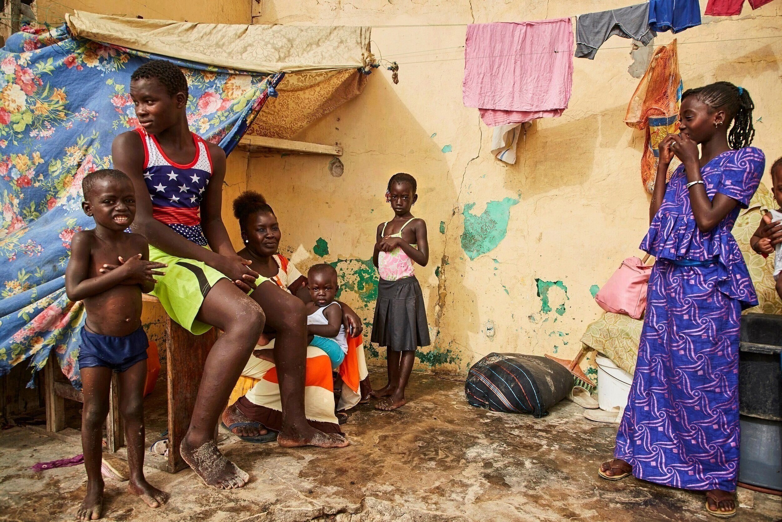  Fatou Ngueye, 34, sits within the last 2 remaining walls of her living room -which is now open to the sand and ocean- with her children. The family has been sleeping on the floor of a neighbor’s home for over a year so that her husband, a fisherman,