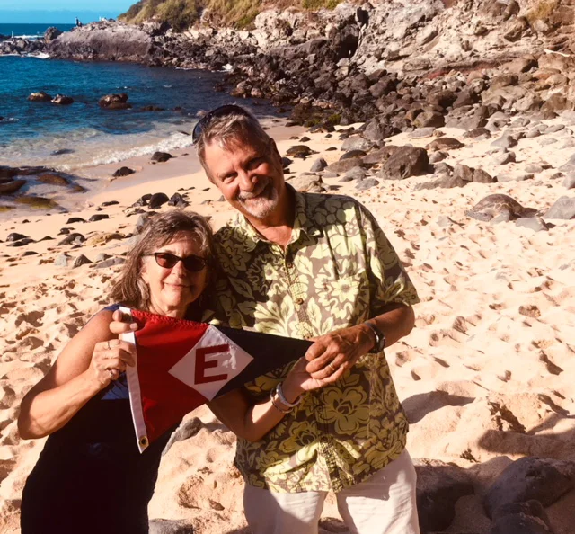 Mark & Sheena Schroeder sport the EYC burgee on a beach in Maui—they note that the 'rocks' behind them are actually sea turtles coming ashore.
