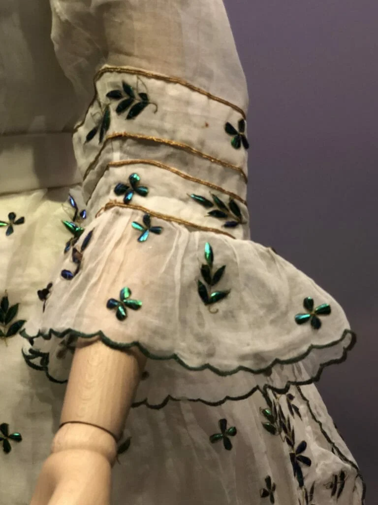 An unnatural use of nature - muslin dress adorned by beetle wings. Muslin day dress decorated with beetle wing cases, 1868-9, Britain. © Victoria and Albert Museum, London.