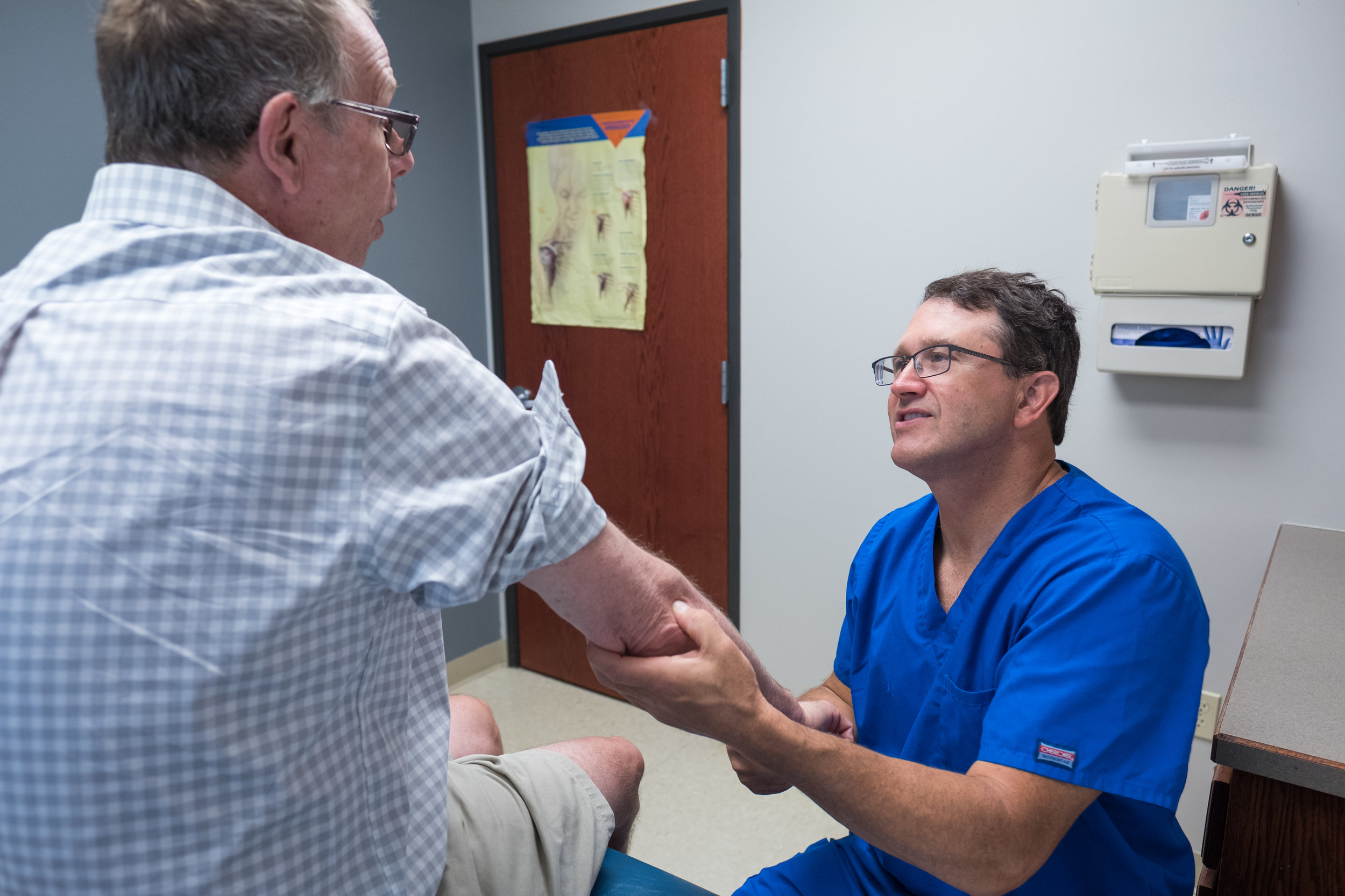  Dr. Galbraith examining Greg's elbow. Greg received a cortisone shot and was diagnosed with "tennis elbow"-likely caused by repetitive movements from sorting and delivering mail. 