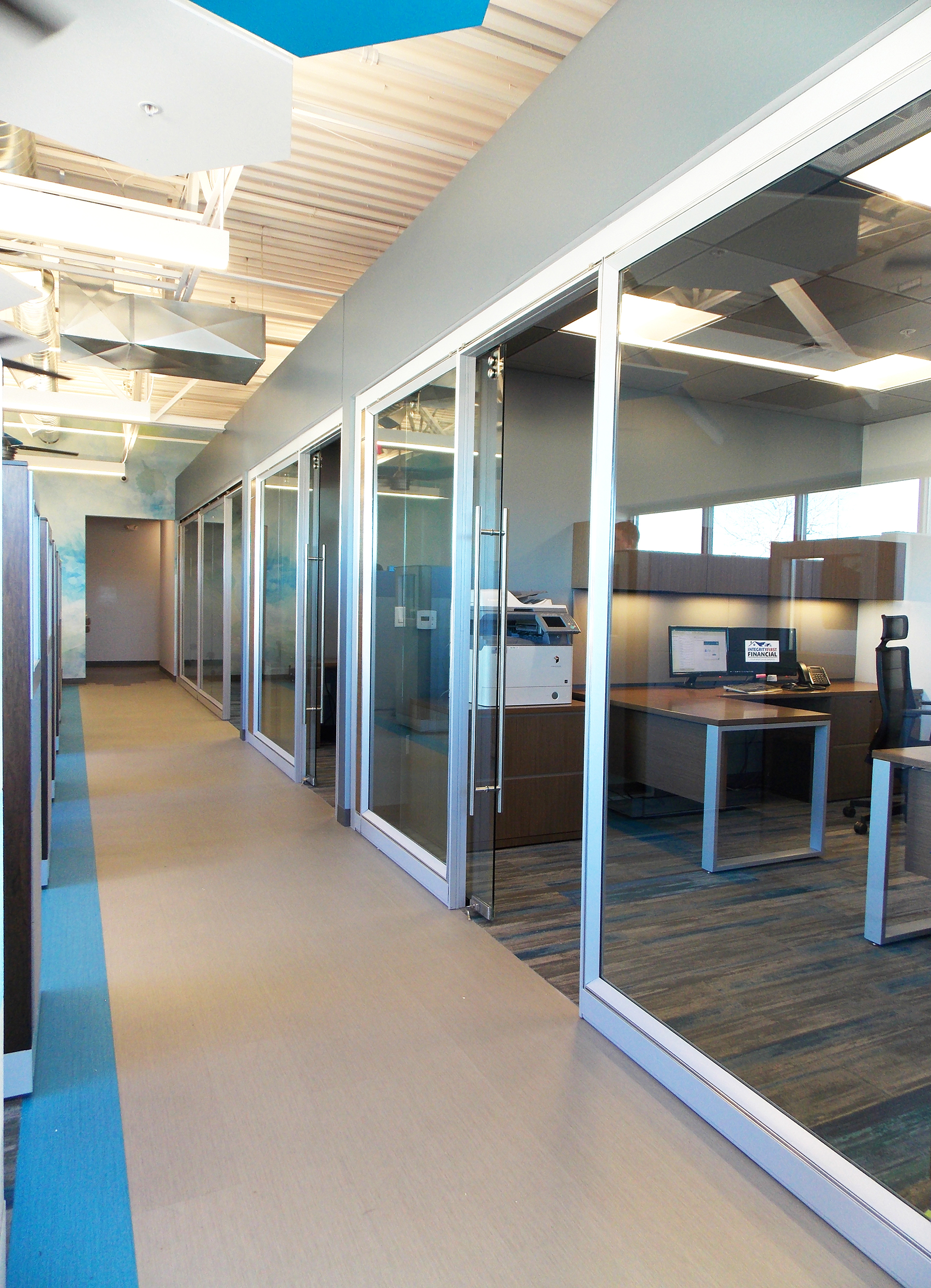 The main walkway separating the private offices from open offices area is Patcraft's Metallix luxury vinyl tile. Throughout the office, it changes between a mix of greys but is accented by a bright blue stripe. The Milliken carpet tiles are primarily grey and accented by blue, but vary in saturation whether you are in the open office or conference room.