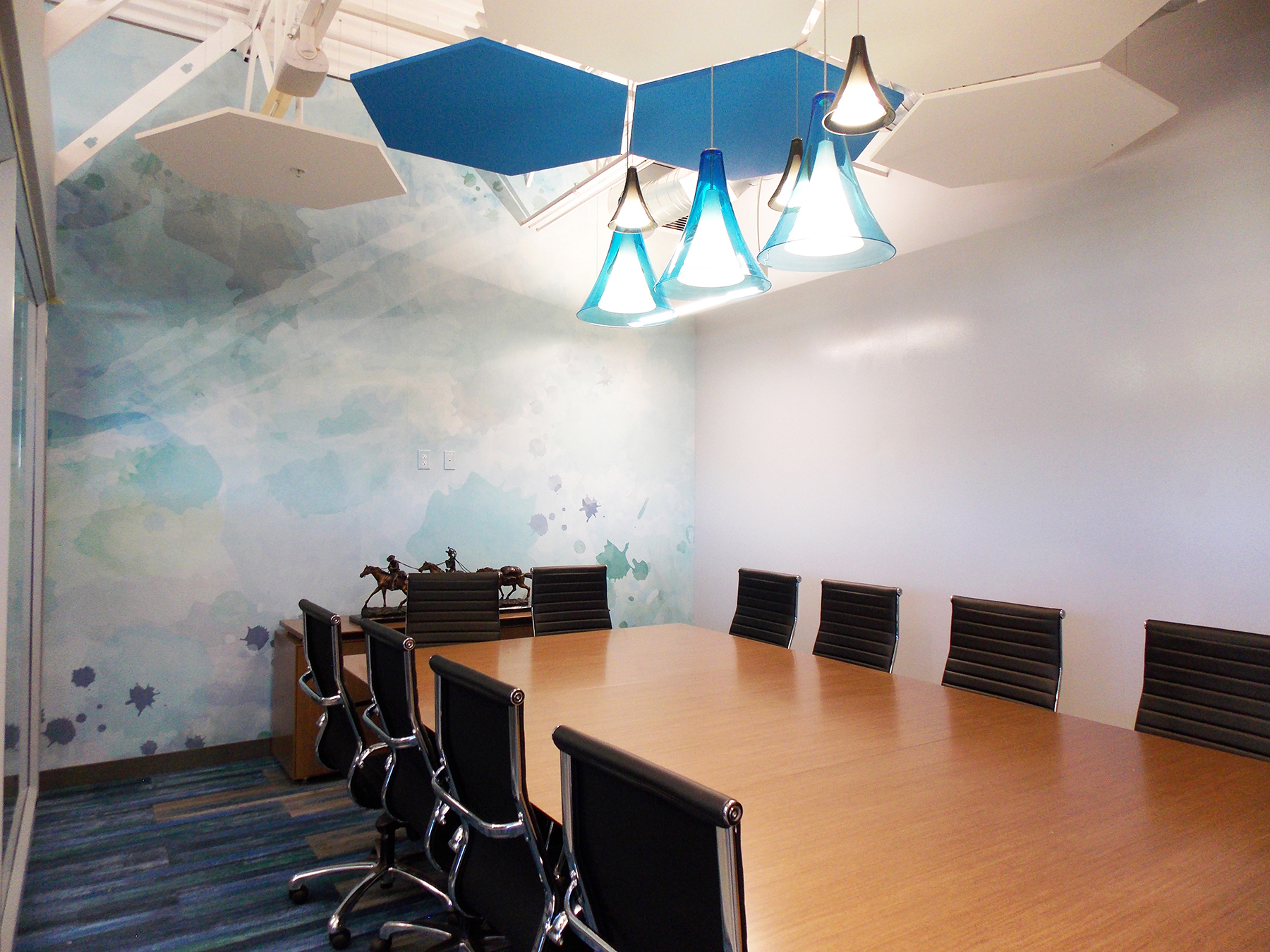 The conference room features special blown glass Tech Lighting fixtures clustered above the conference table for a significant impact. They are accented in place by Armstrong Soundscapes clouds and an original watercolor wall graphic that stretches across the back wall created by Angela Harness, one of our very own designers.