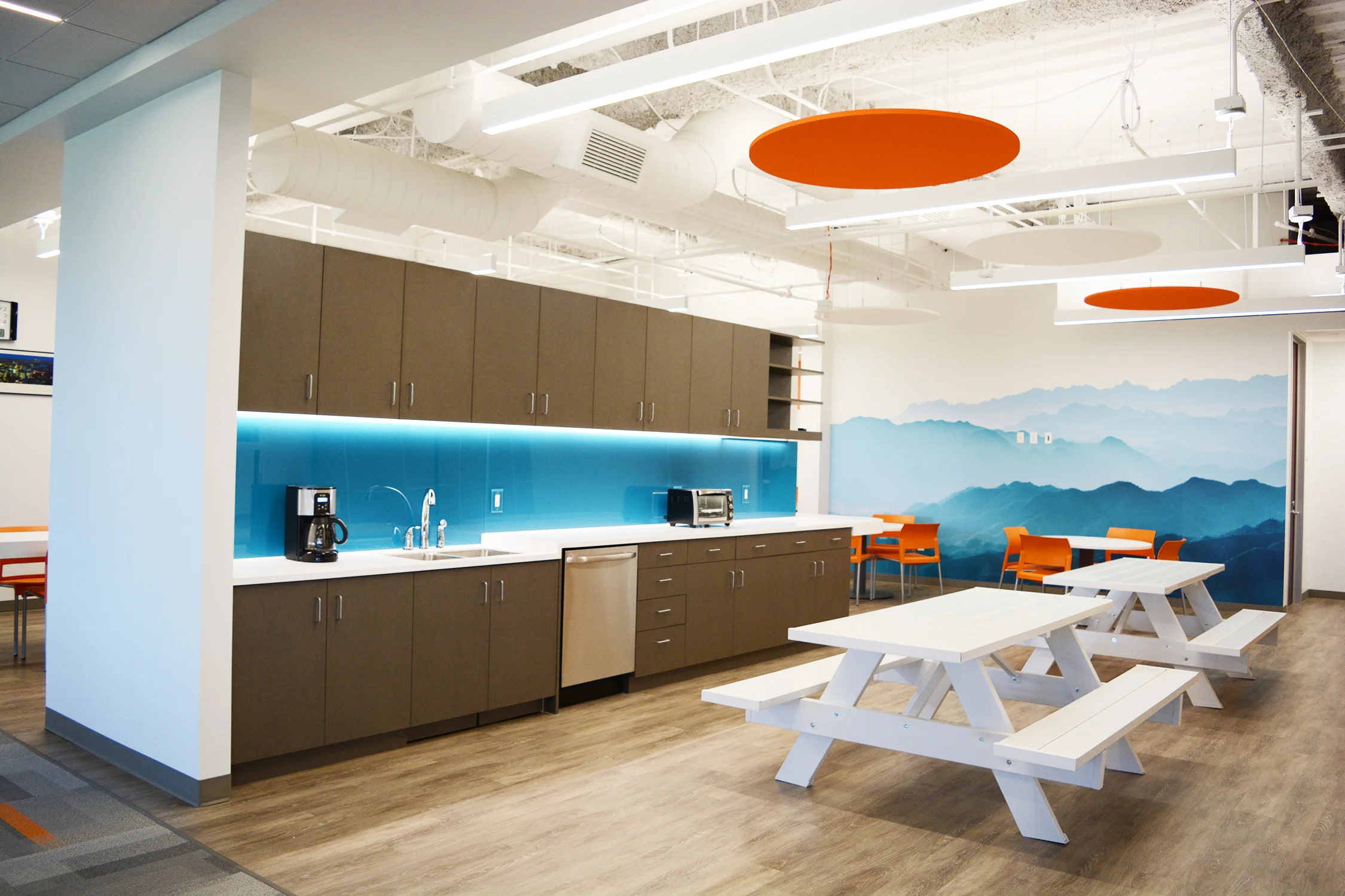 The double sided break room wall divides the space to allow for multiple zones of seating and furniture types, provided by Officescapes . The picnic tables add a great regional touch as well as a functional aspect to the room. A large mountain scene graphic on the back wall anchors the space and adds depth, color and wonder.