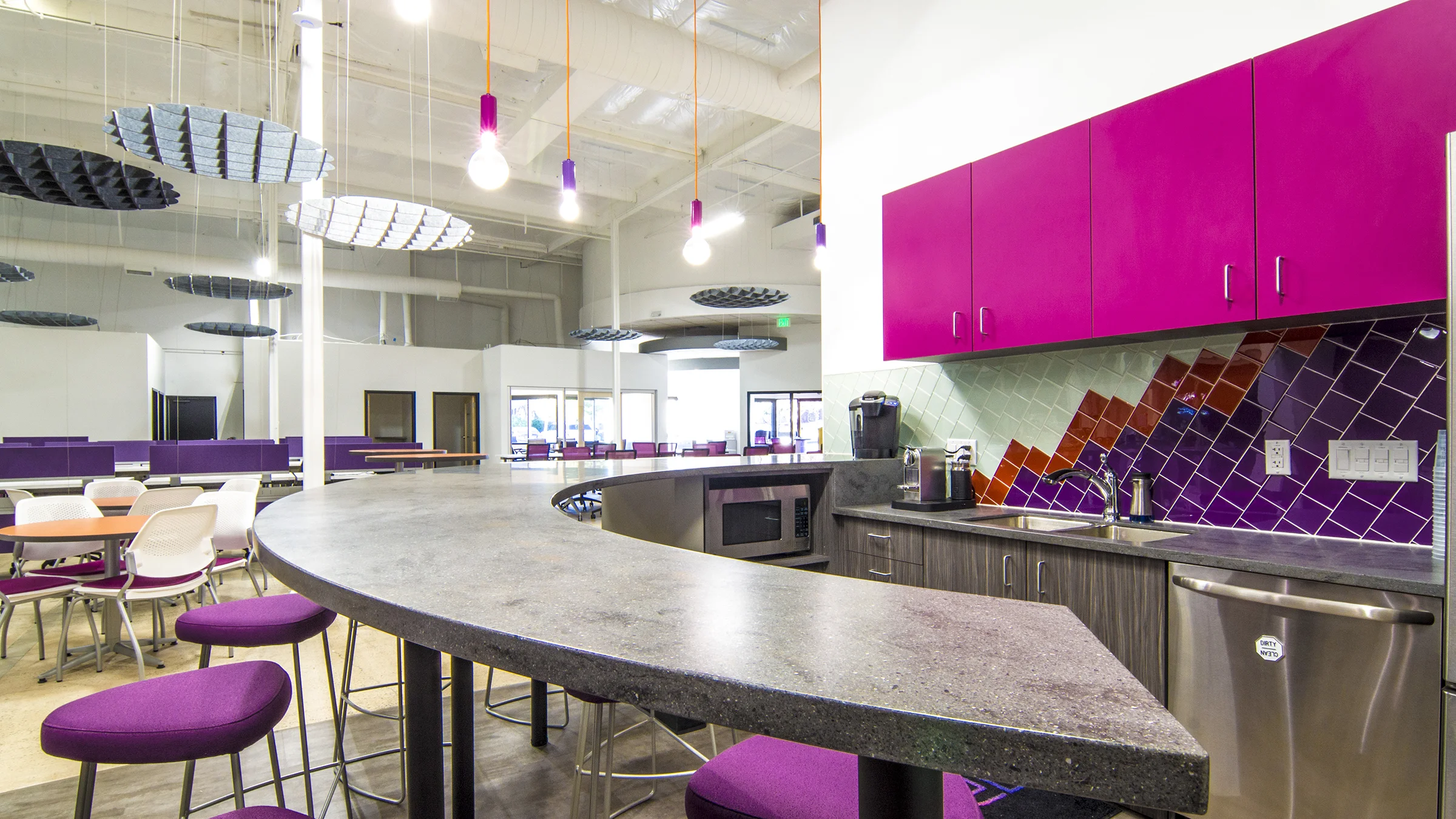 An important part of the space was the break room. The bar top design was a feature incorporated from the very first space plan in a different location. The tile backsplash was created from Crossville Glass Blox ; by angling the tile, a sense of the mountains to the west was incorporated into the space. To add a punch, the pendant lights provided by Visual Interest were selected because of the ability to inject the brand colors. 