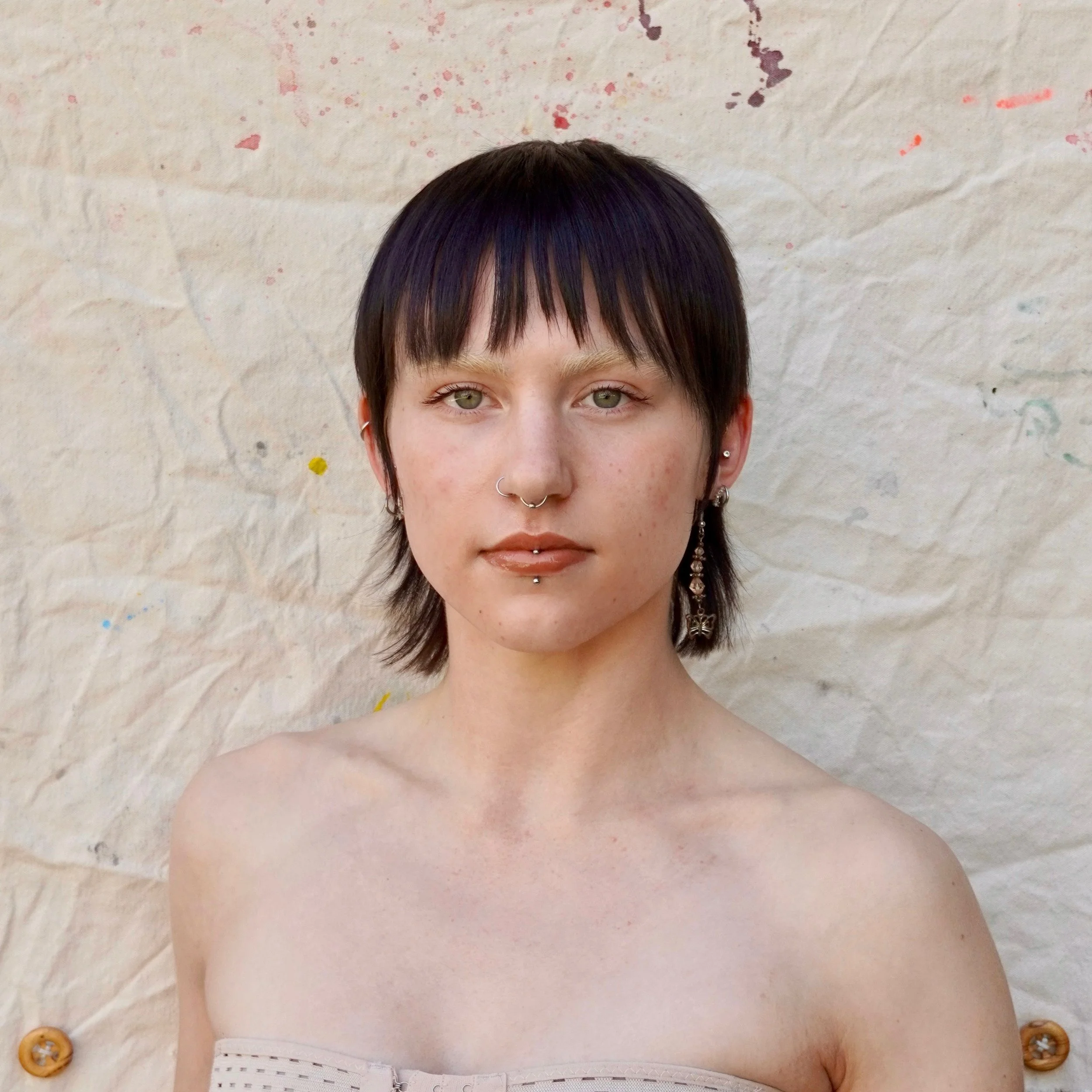 Mads looks toward the camera with a Mona Lisa-esc smile. They have light skin and straight dark hair that falls to just below the chin.