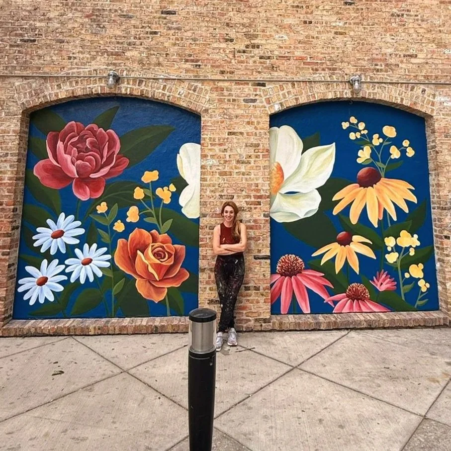 Ryan Tova Katz smiling and standing in front of her floral Old Town exterior mural in Chicago