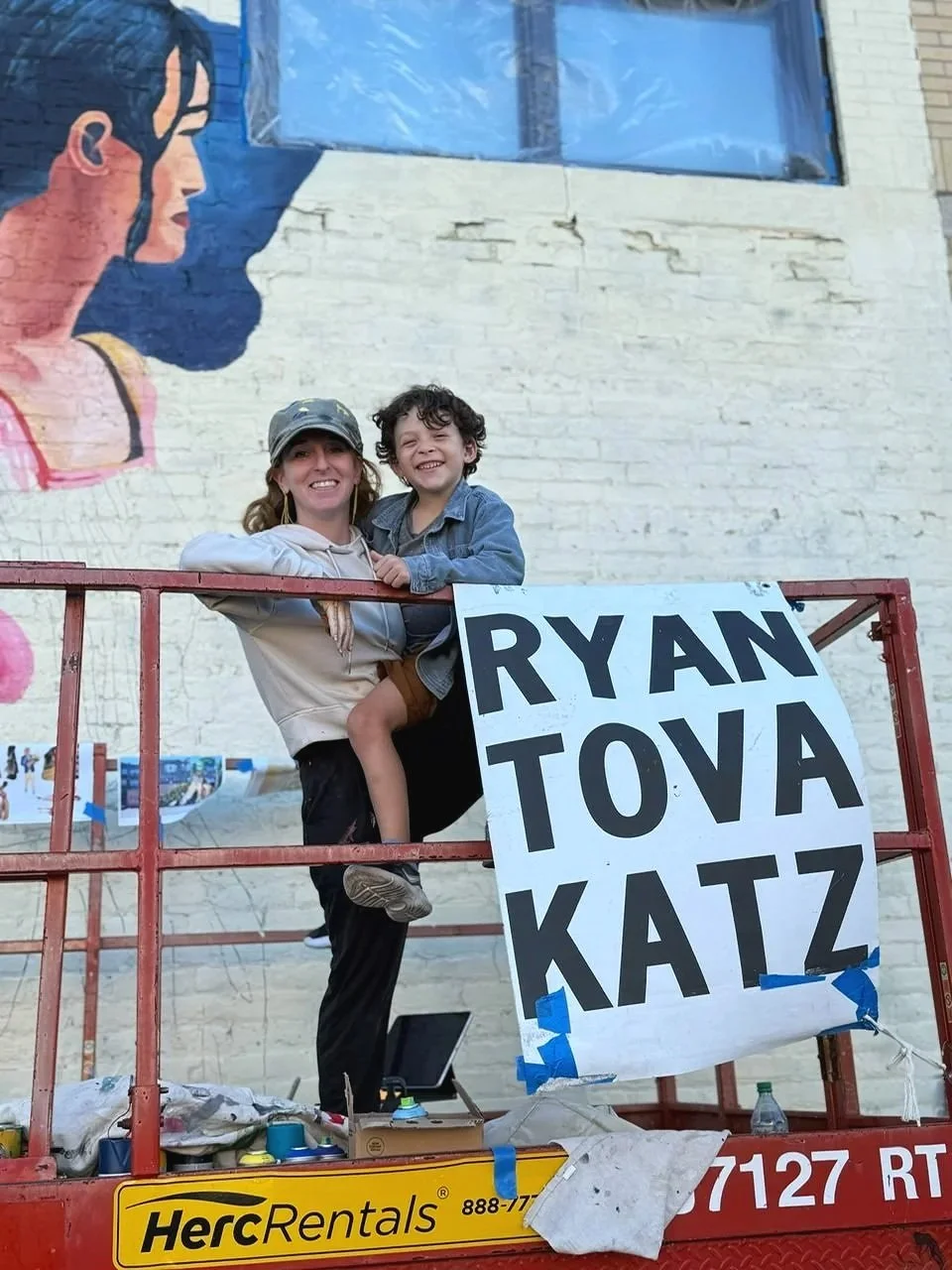 Ryan Tova Katz working on Rogers Park Chamber of Commerce mural on a lift with her son in Chicago