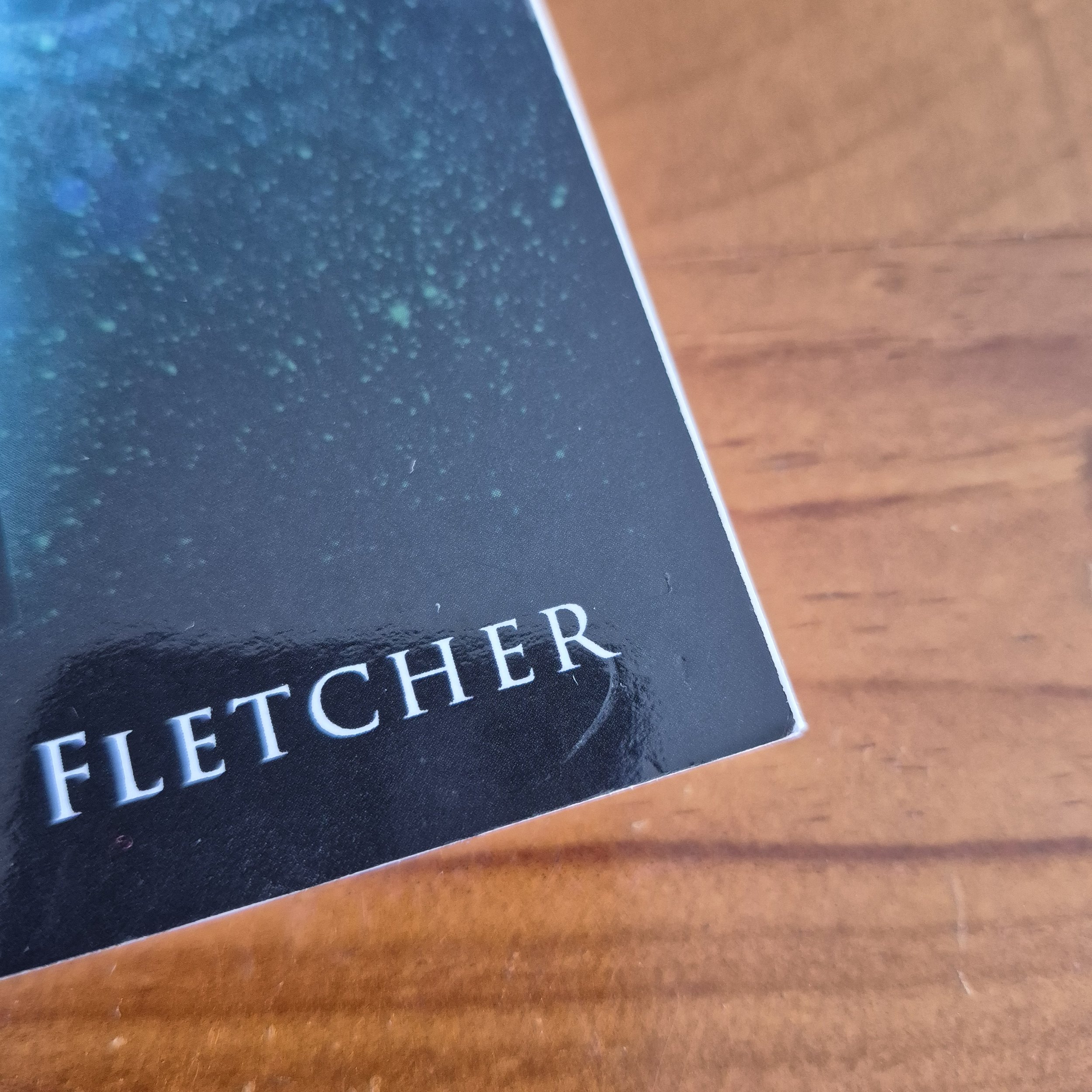 The corner of a book against a wooden background. There is a slight scratch on the front cover near the corner.