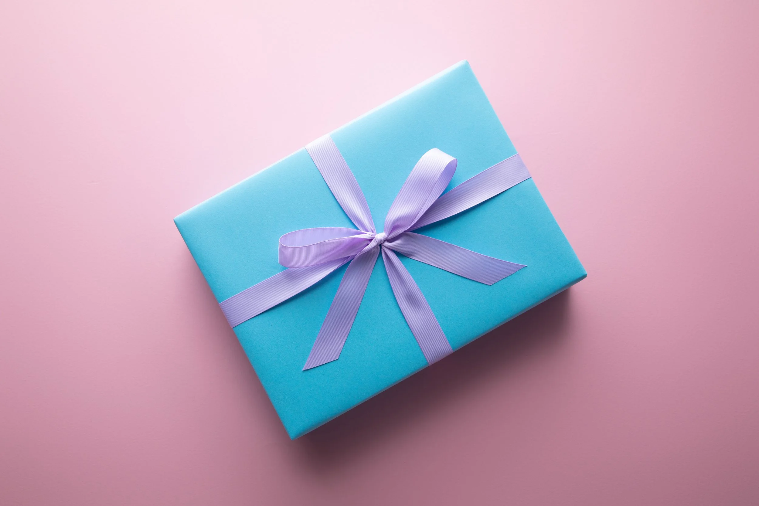 A present wrapped in blue paper with a purple ribbon on a pink table.