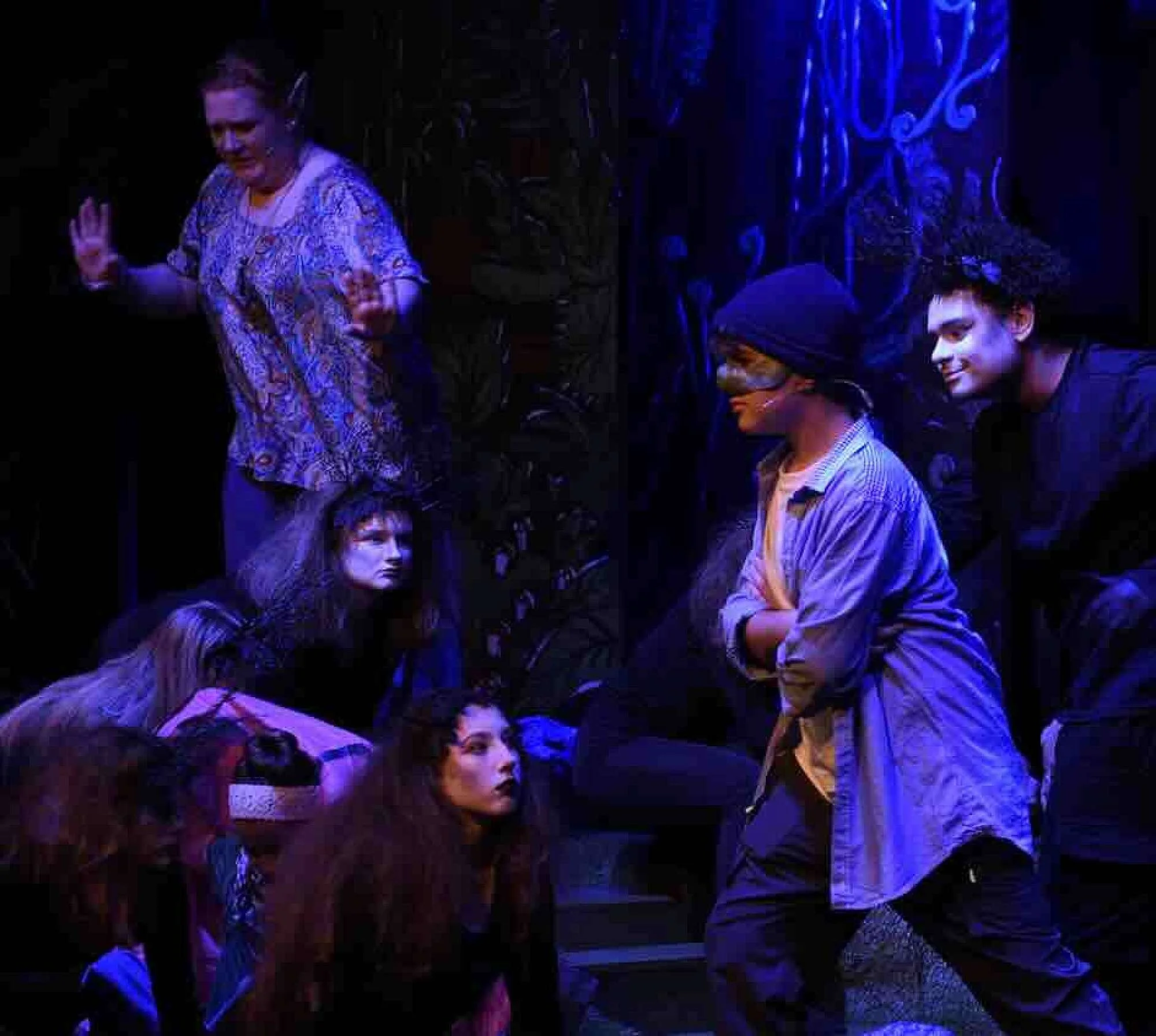 A group of young performers on a stage. Several of them are covered in face paint, making them look like creatures. The stage is bathed in blue moody lighting.