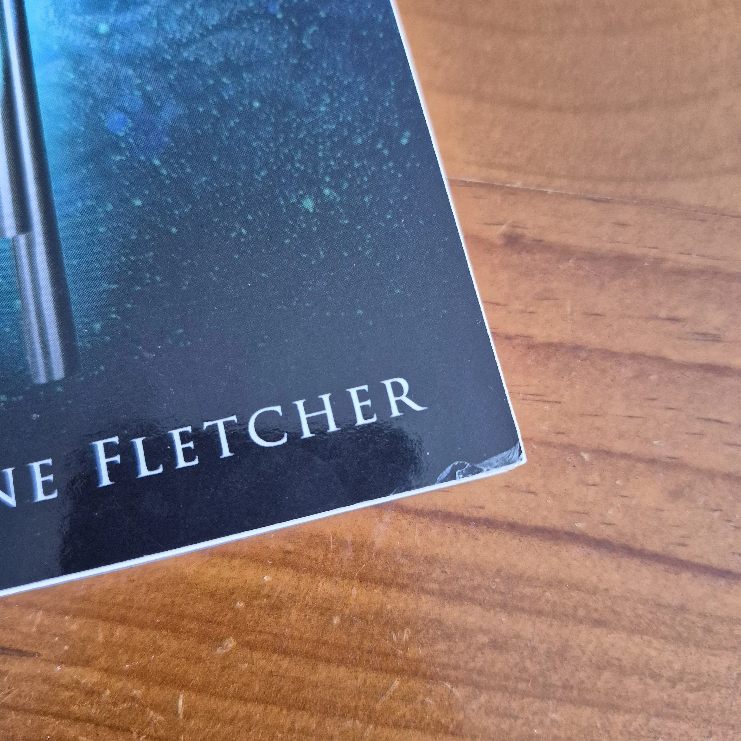 The corner of a book against a wooden background. The lamination is pulling away from the cover slightly at the corner.
