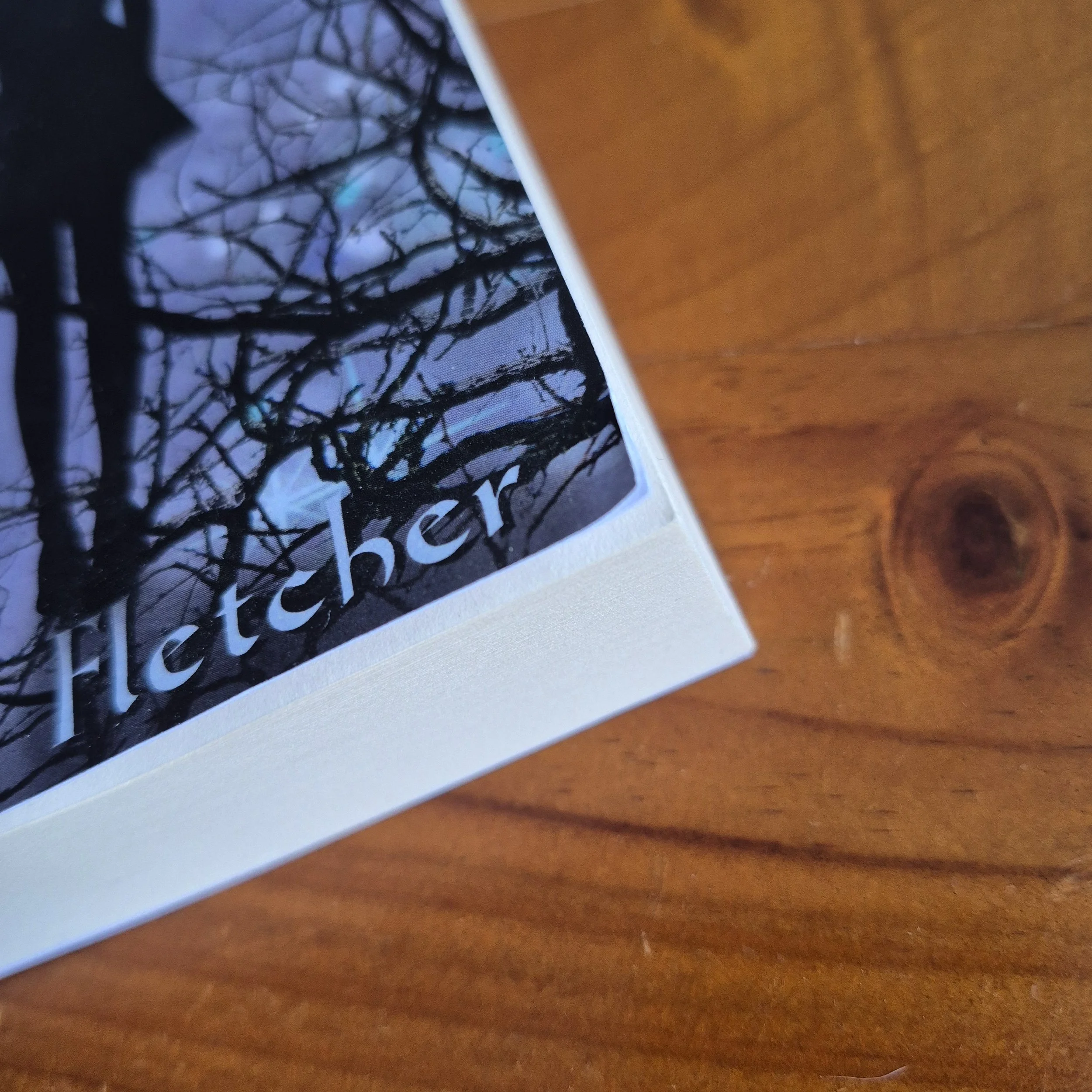 The corner of a book against a wooden background. The corner is bent slightly, damaging the edge.