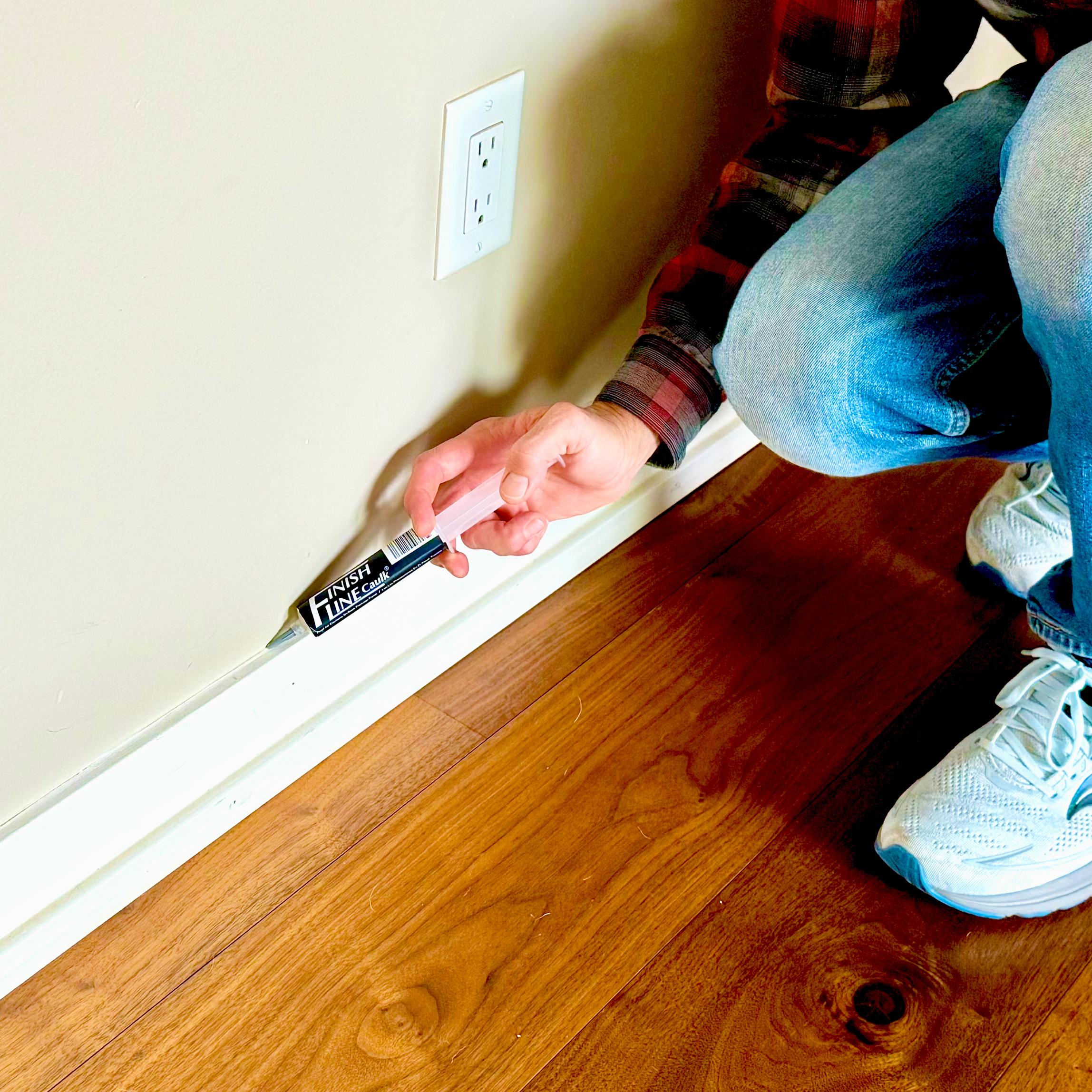 Applying precision caulk along wood baseboard and quarter round trim using a Finish Line Caulk applicator for clean, controlled lines.