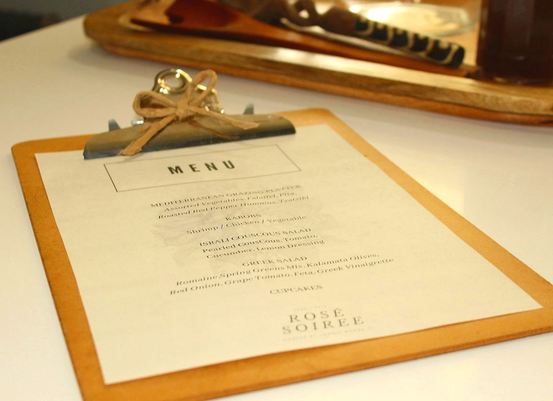 The Menu I designed the menu using Canva.com. I printed it out on eggshell paper and attached it to a clip board for a casual vibe. I embellished the clipboard by making a bow out of the handle of a brown shopping bag . Once I formed the bow I attached it with a bit of hot glue.