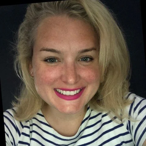 Woman with blonde hair smiling, wearing a striped shirt, against a dark background.